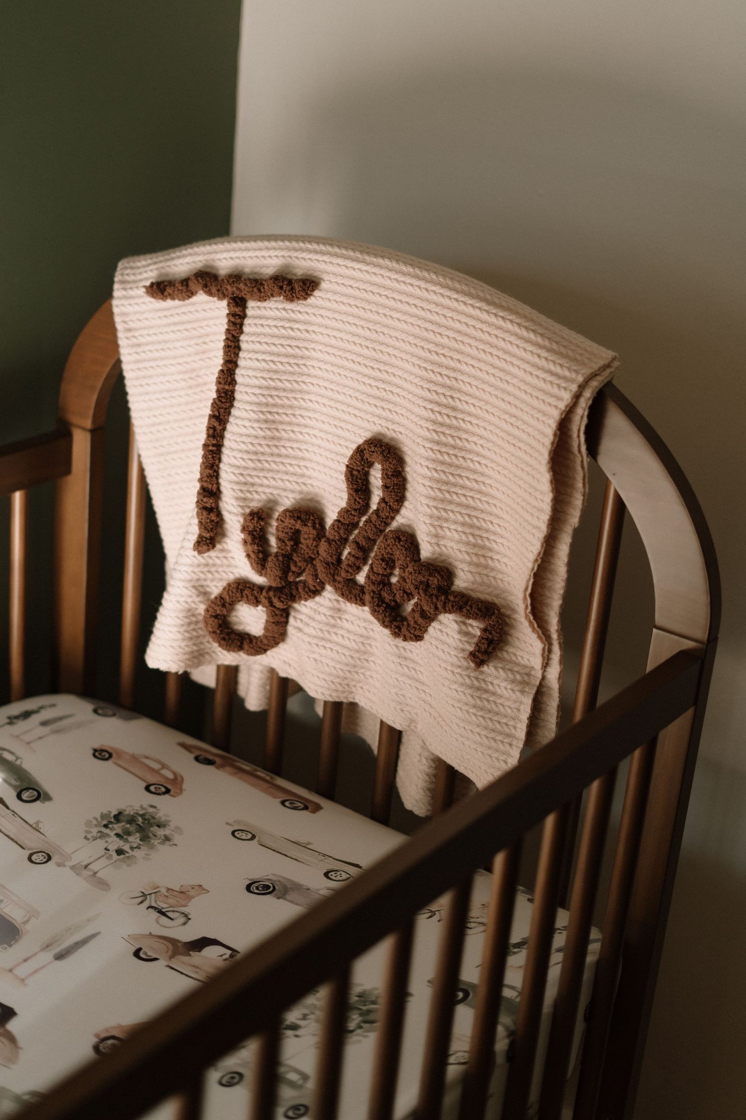 Brown knit blanket draped over wooden crib with animal themed bedding.