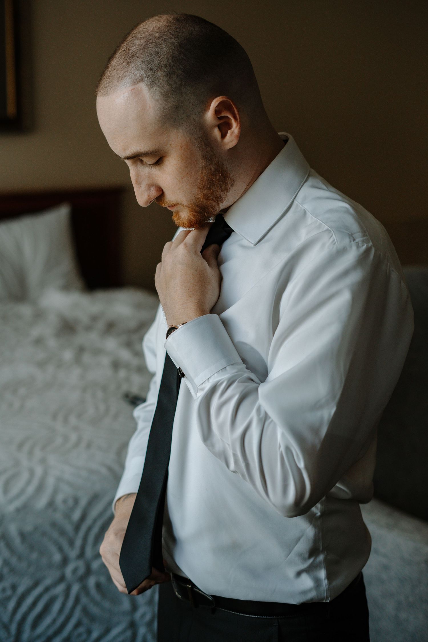 Groom in white dress shirt and tie adjusts their collar while getting ready.