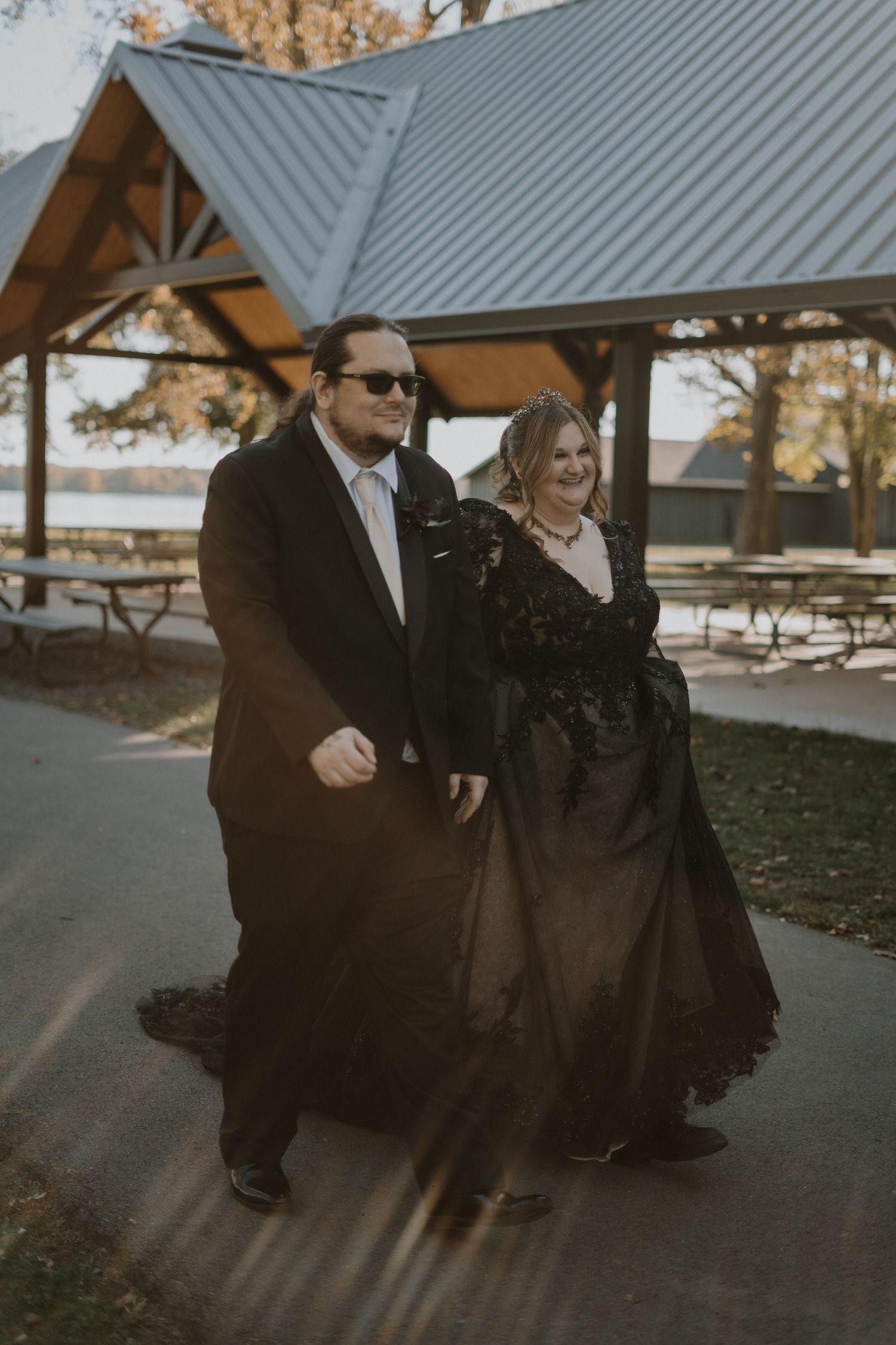 A couple walks on a path under a metal roof structure during a photo session.