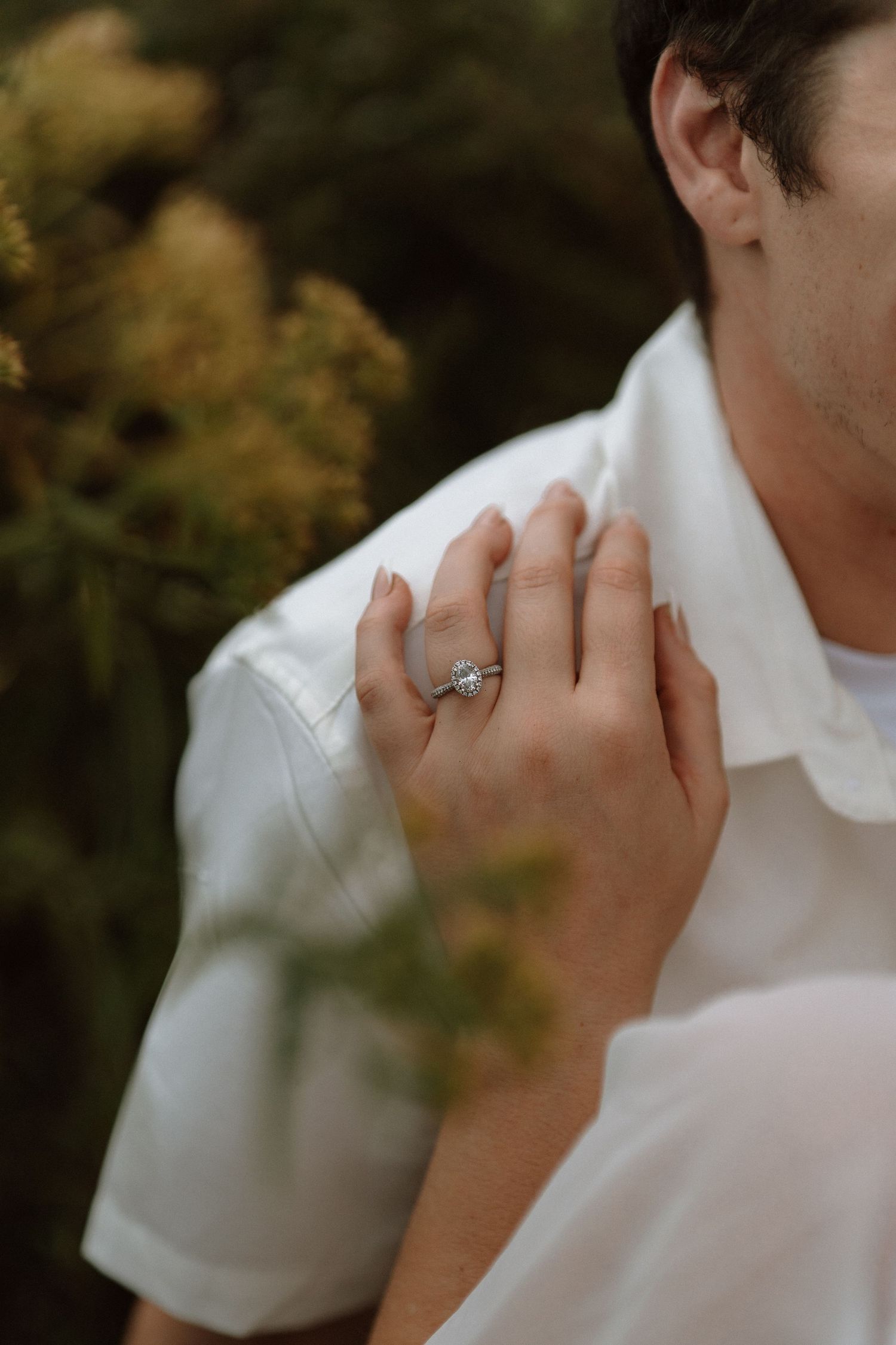 Close-up sequence of a person wearing a white shirt and ring touching their face in a natural outdoor setting.