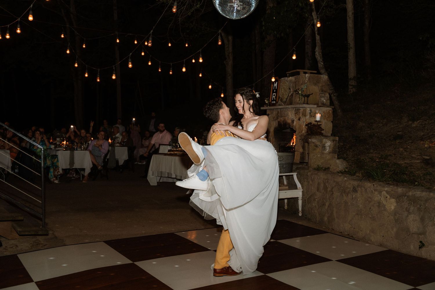 Bride and groom share a romantic first dance on checkered floor at outdoor evening wedding reception.