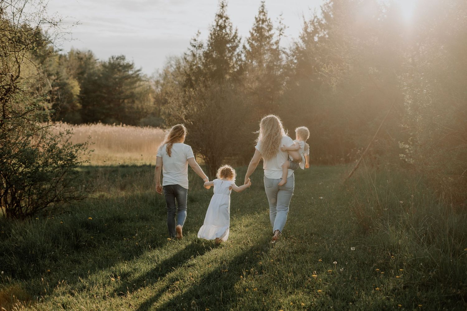 Family walking together through sunlit meadow during golden hour.