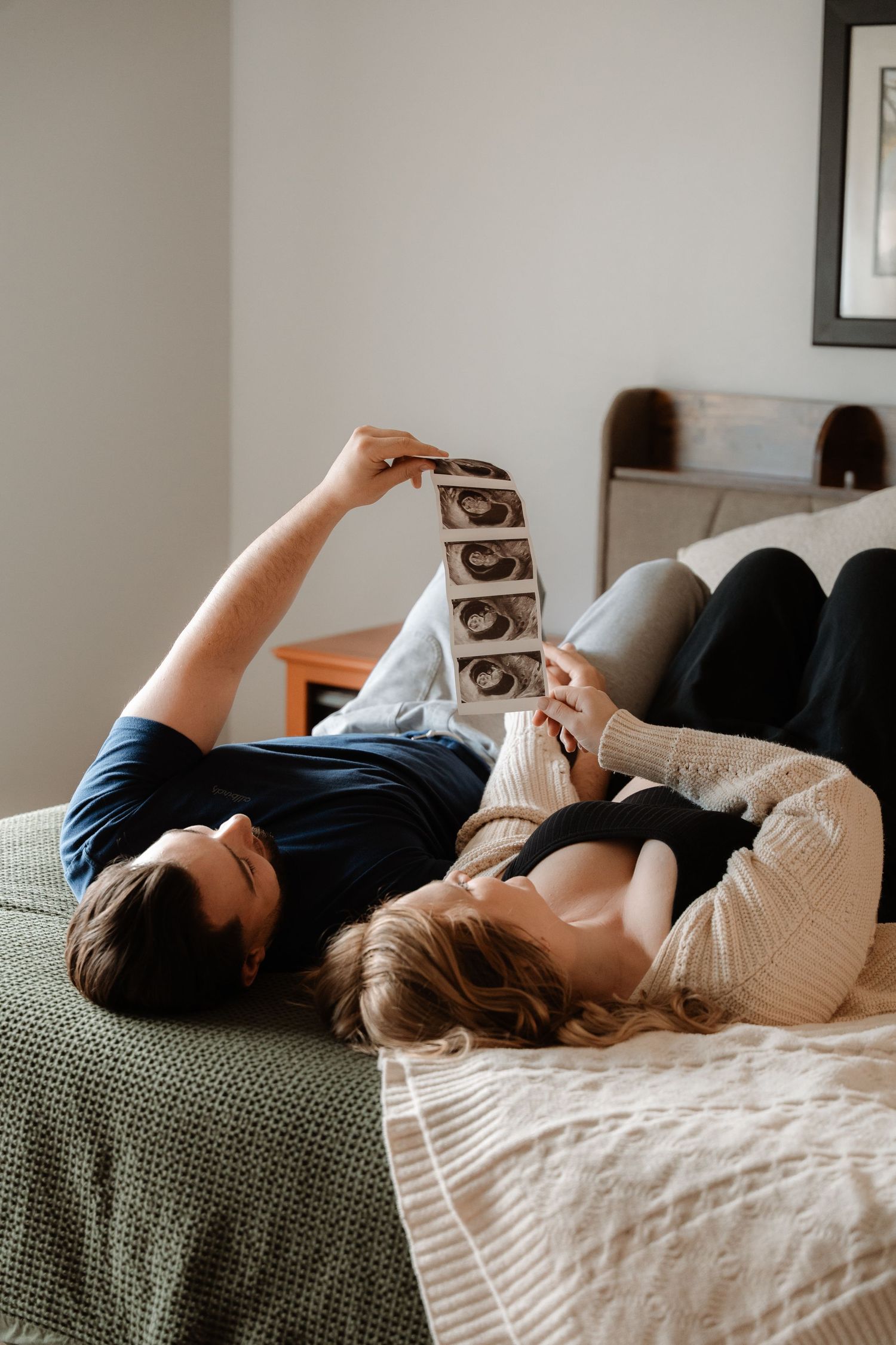 Couple lying on bed together reviewing ultrasound photos, expecting parents sharing a tender moment at home.
