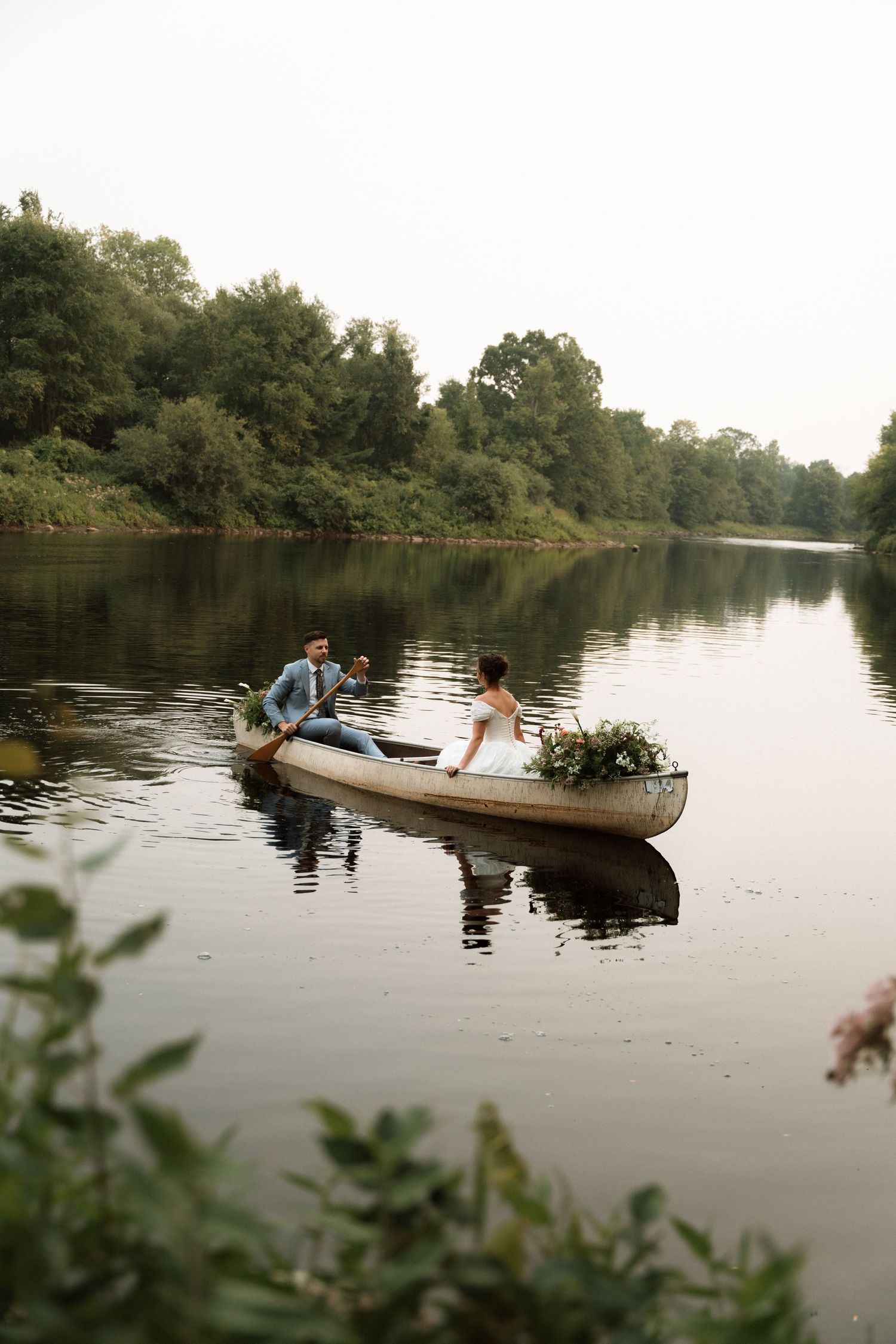 People enjoy a peaceful canoe ride on a calm river surrounded by lush green trees on a tranquil summer day.