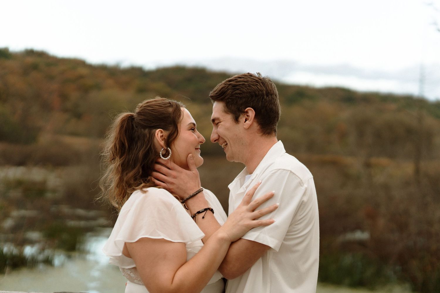 A couple embraces in a romantic moment against a scenic mountain backdrop during their engagement photo session.