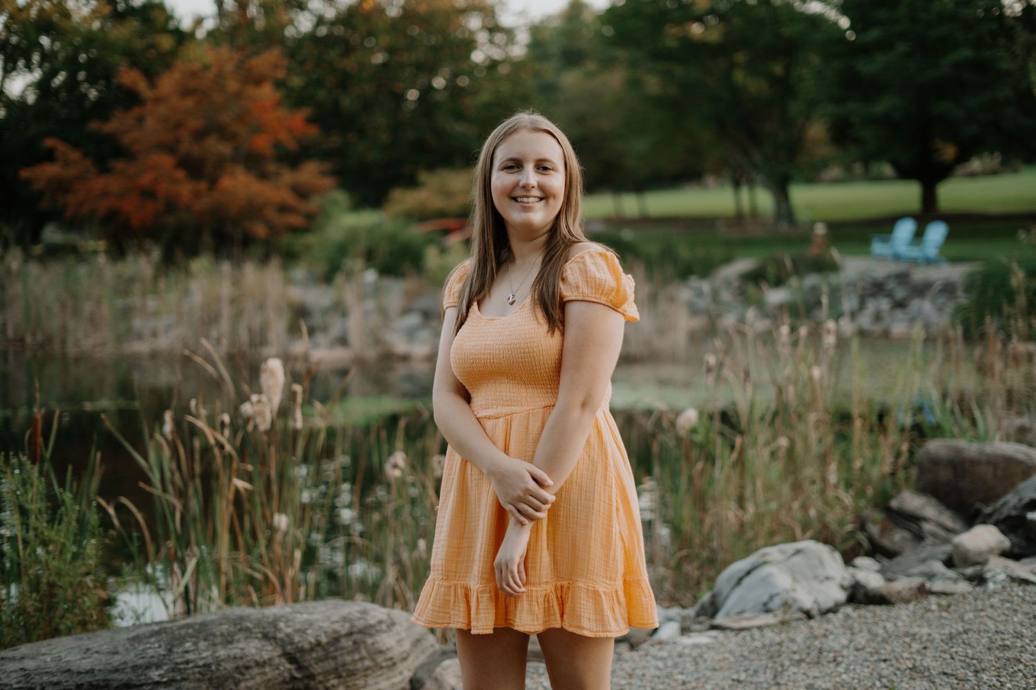Person wearing a peach-colored dress standing in a field with autumn foliage.