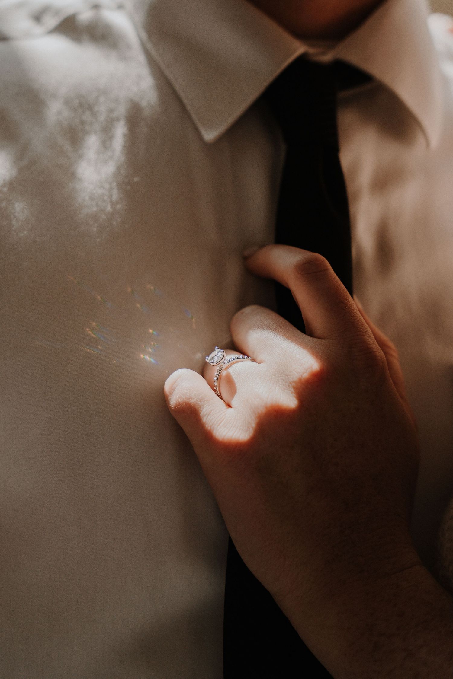 Close-up of sparkling engagement ring against white shirt and black tie.