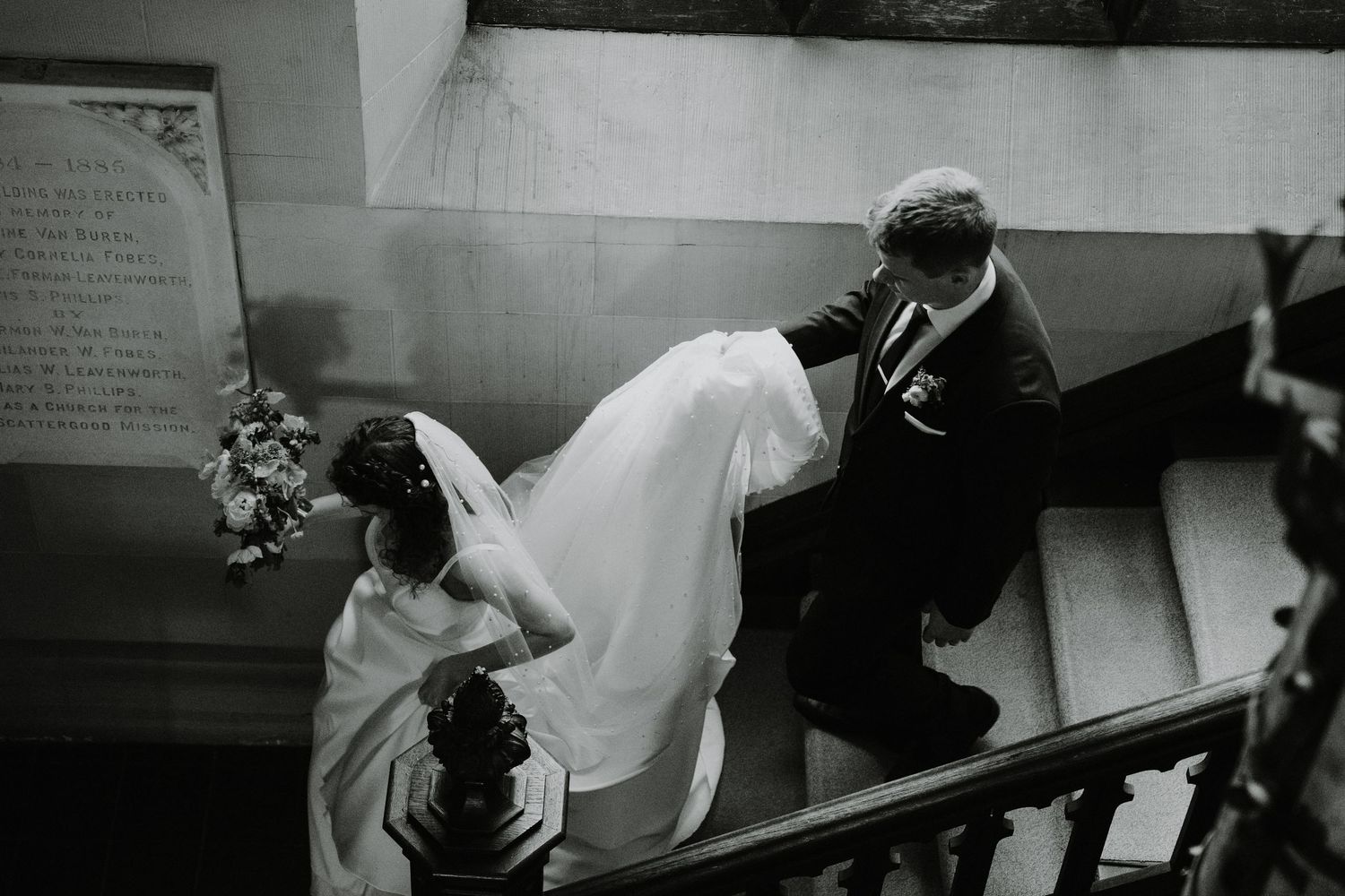 Bride and groom ascending vintage staircase in black and white photography.