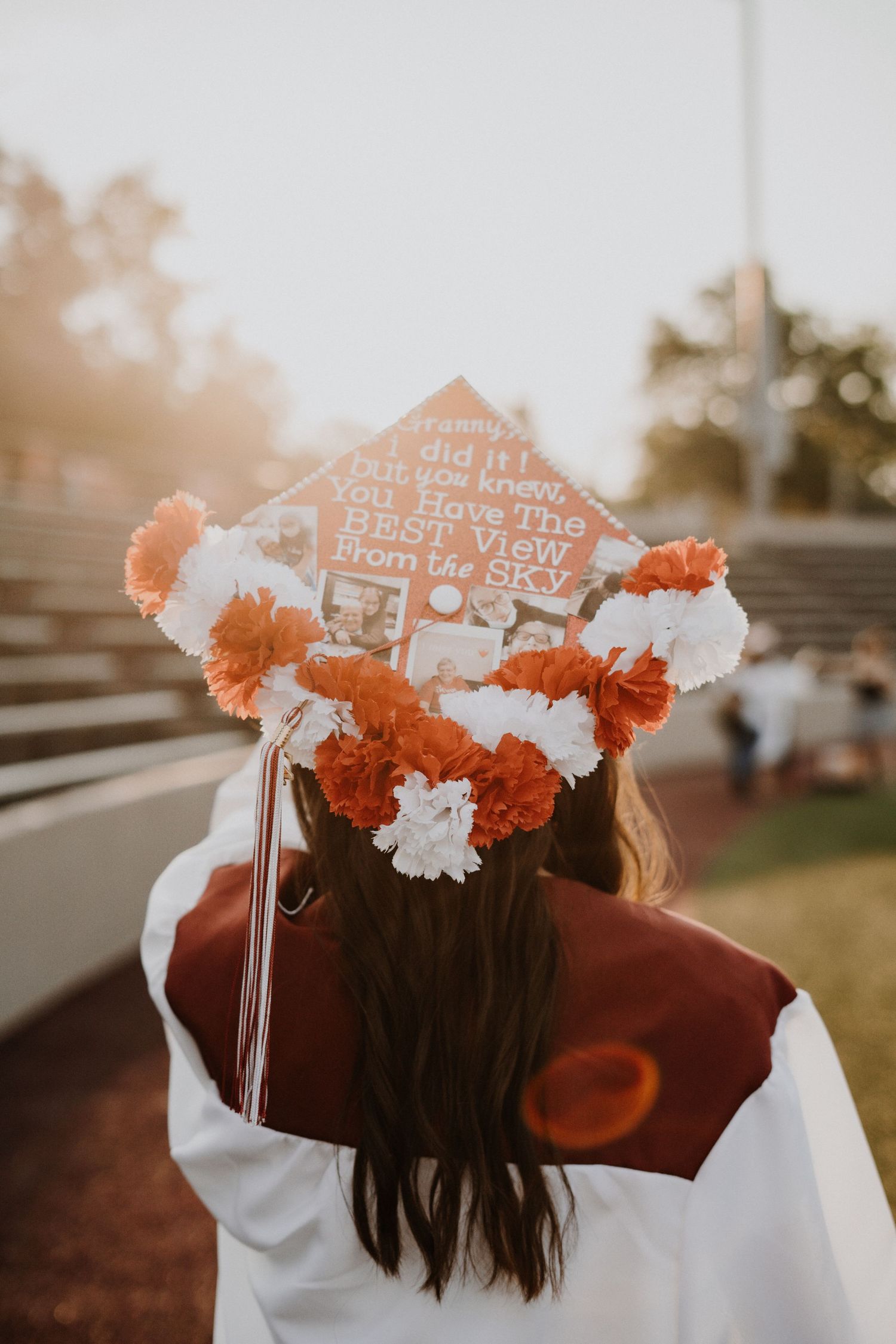 Graduation cap decorated with orange flowers and text photographed from behind.