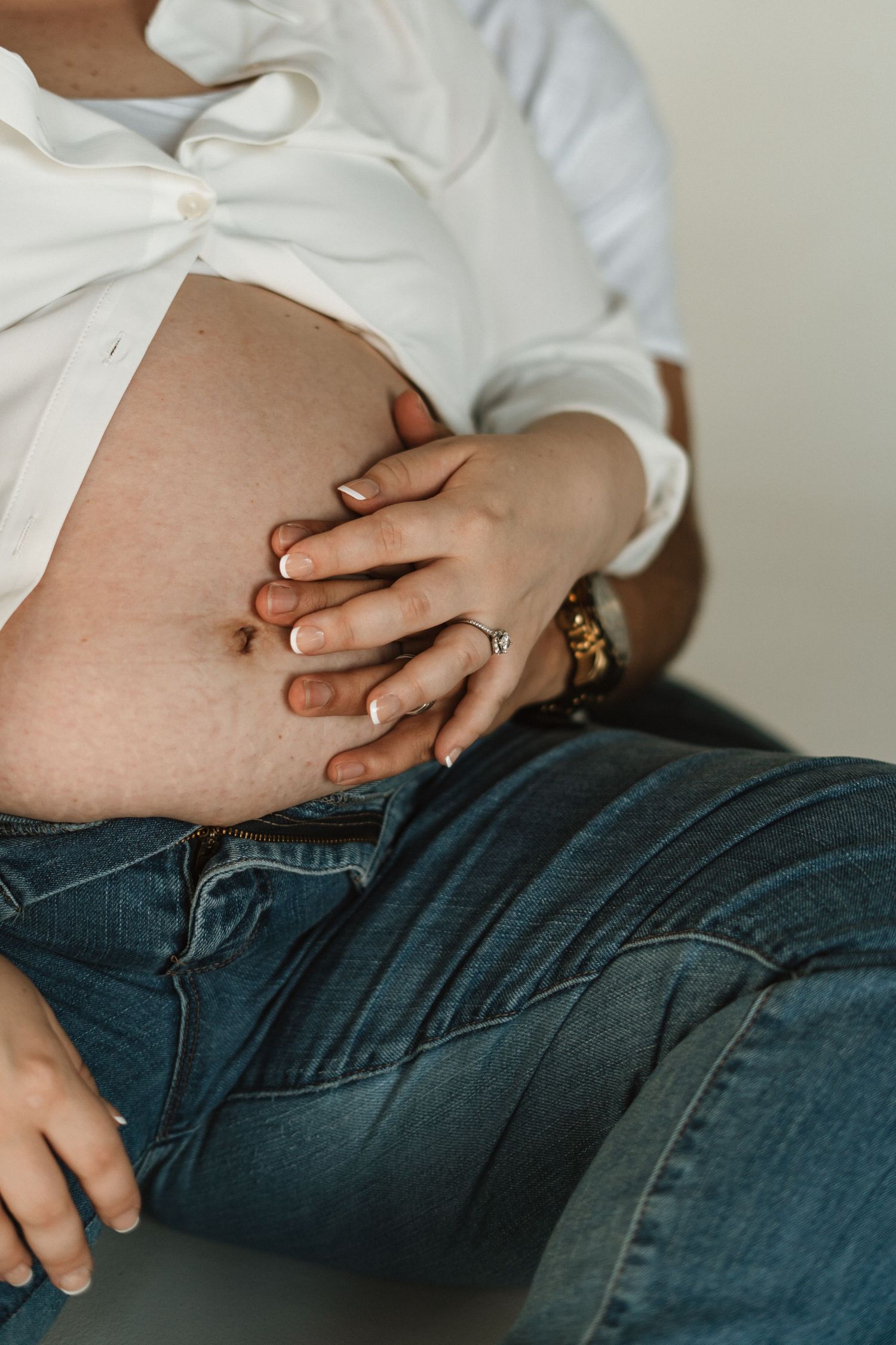 Close-up view of hands resting on a pregnant belly wearing blue denim jeans.