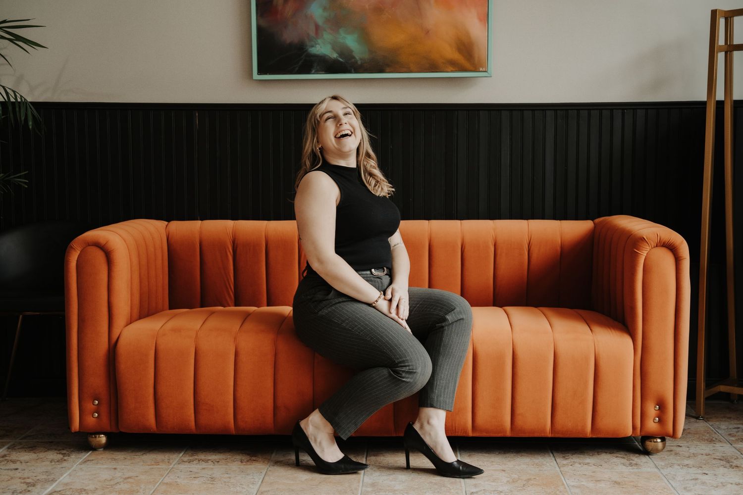Headshot of woman sitting on an orange velvet couch in front of abstract wall art.