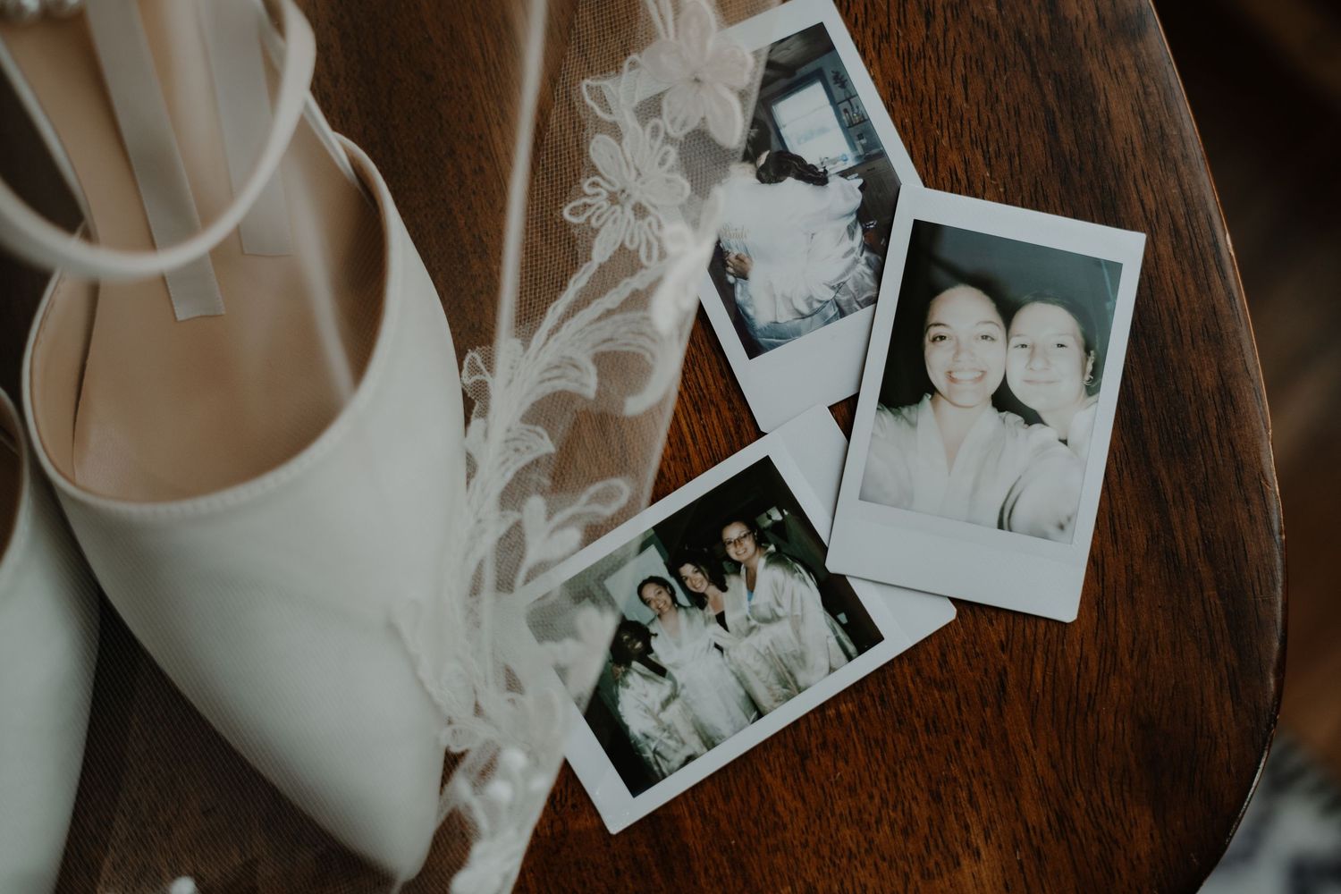 Vintage photographs and bridal shoes arranged on dark wooden surface in moody lighting.
