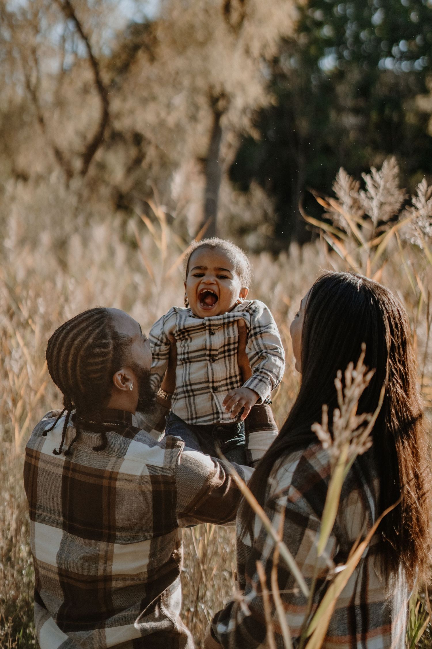 A joyful moment captured in a field of tall grass with coordinating plaid outfits on a sunny autumn day.