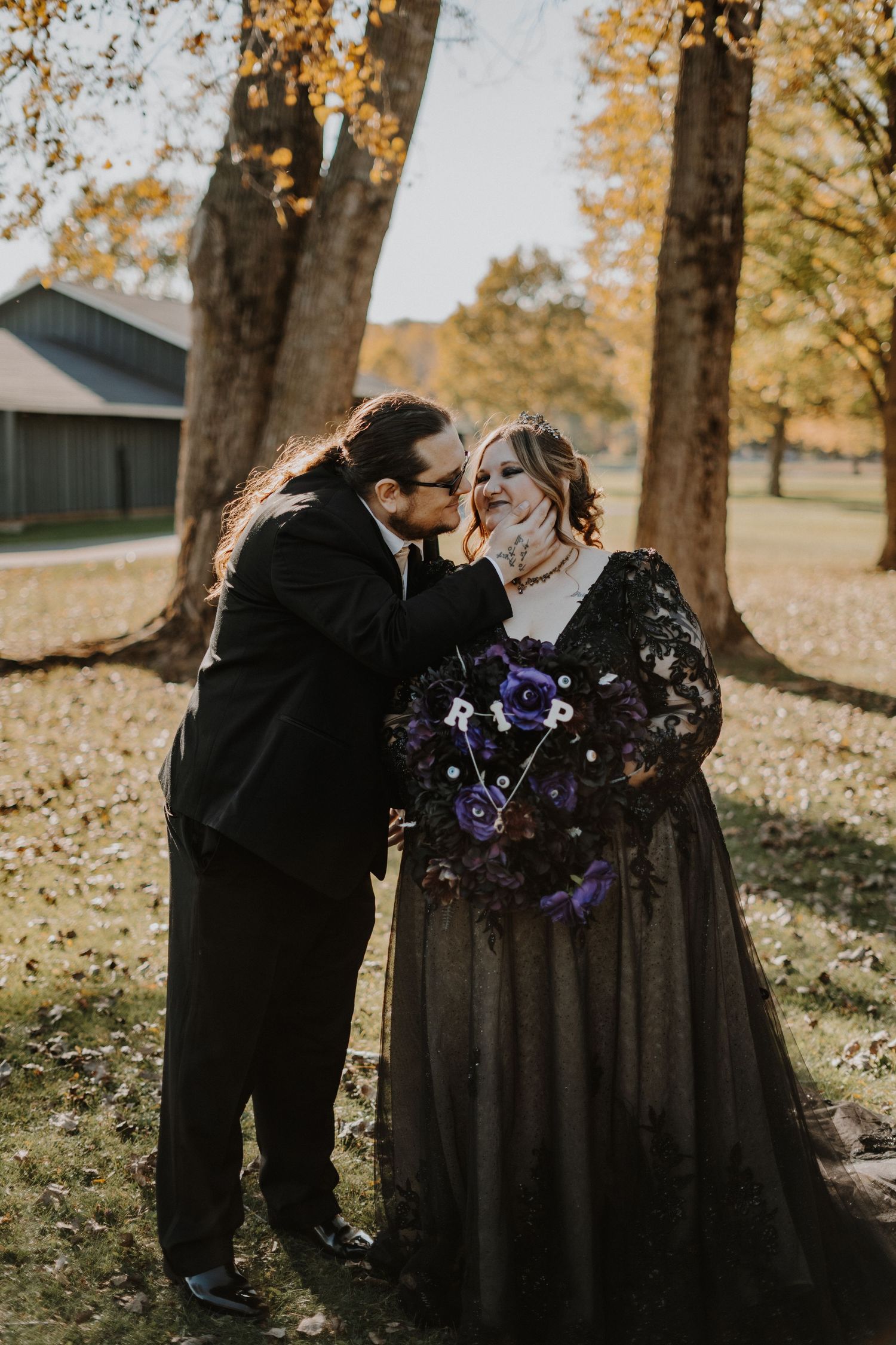 Romantic autumn wedding portrait with couple among fall foliage and purple bouquet.