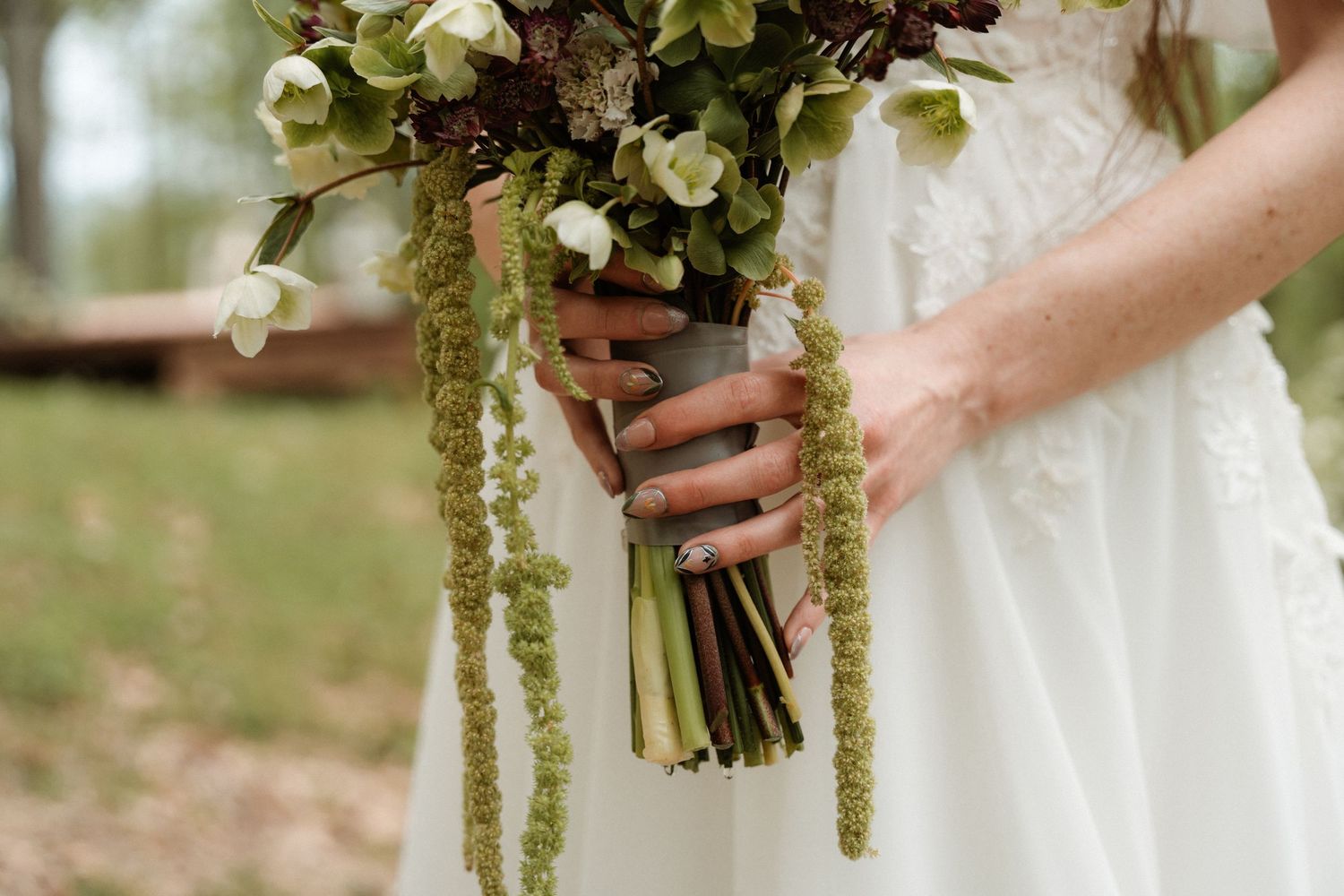 Bride in white lace dress holding a lush wedding bouquet with green amaranthus and white flowers.