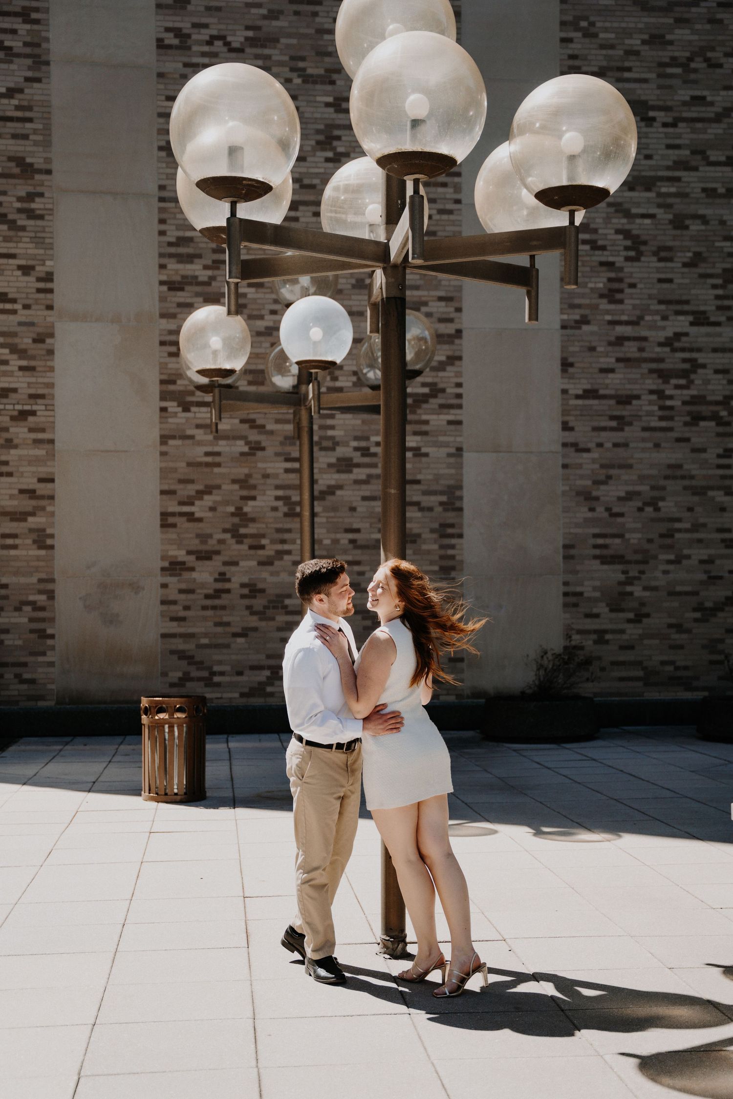 A romantic couple shares a moment under ornate globe light fixtures against a textured wall background.