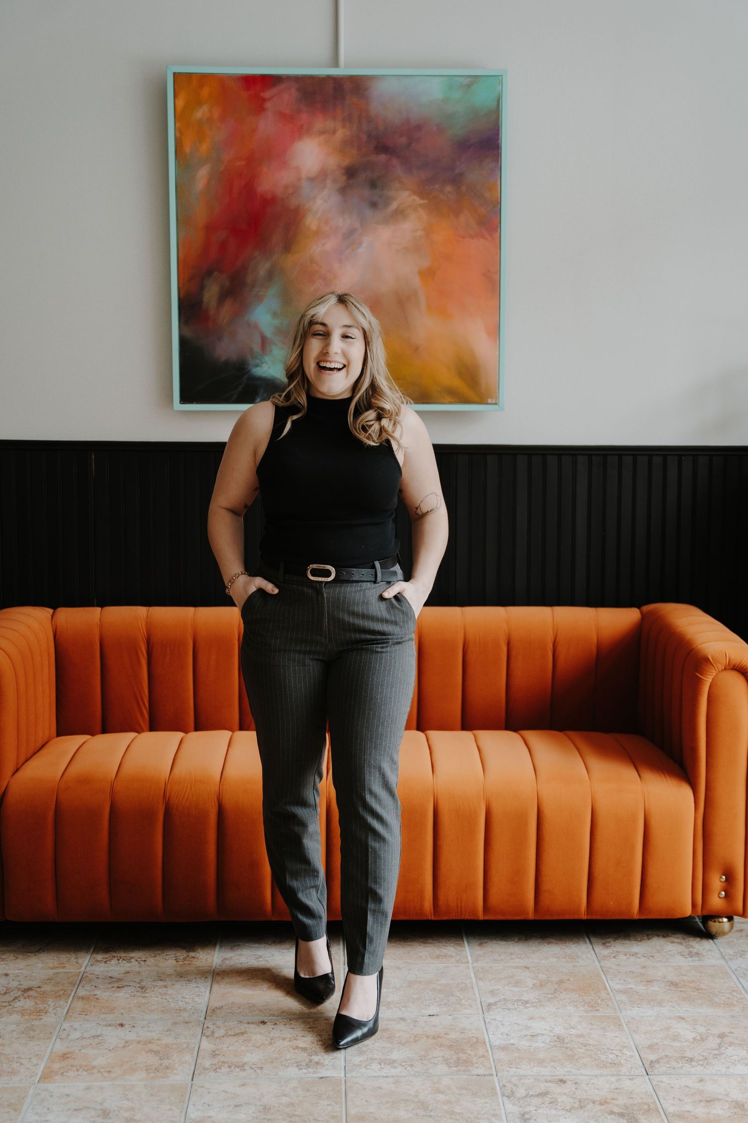 Headshot of a person standing and smiling in front of colorful wall art and orange couch.