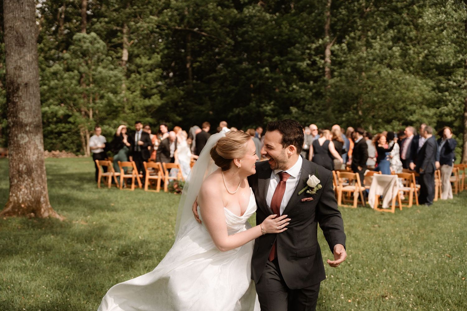 Bride and groom share a joyful moment walking away from an outdoor wedding ceremony surrounded by guests.