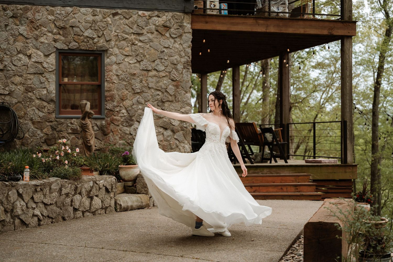 Bride twirling in white wedding gown outside rustic stone venue surrounded by lush greenery.