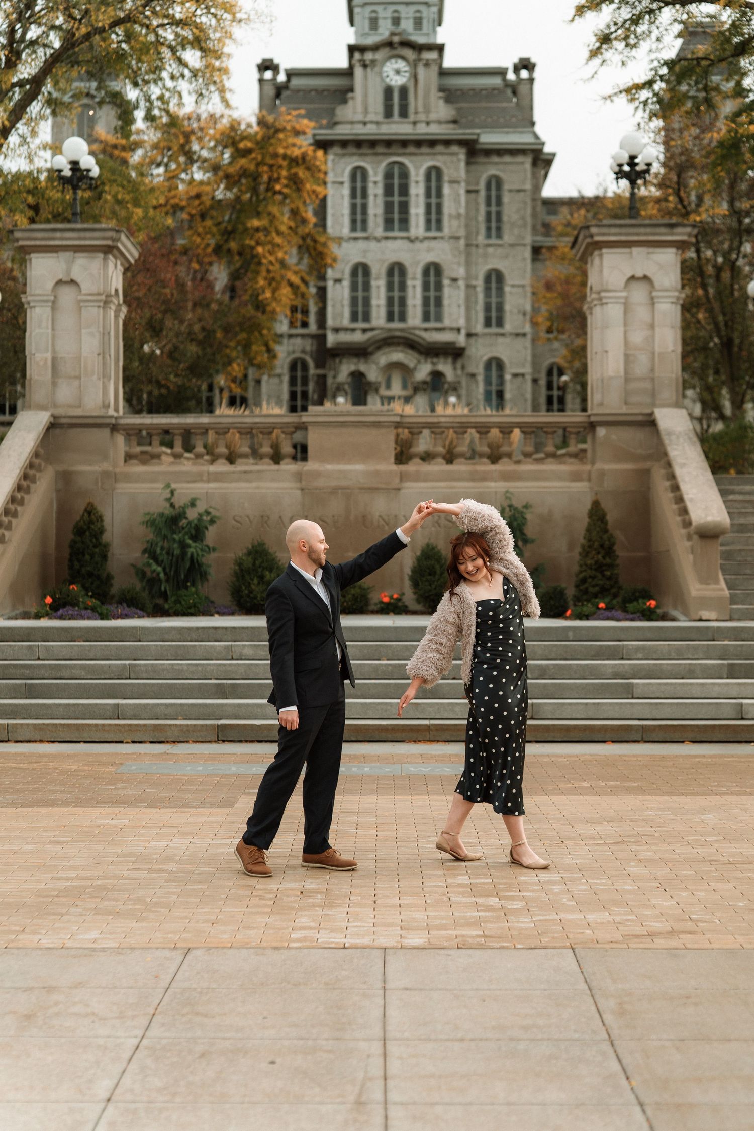 Couple dancing outdoors in front of a historic stone building with grand staircases during autumn.