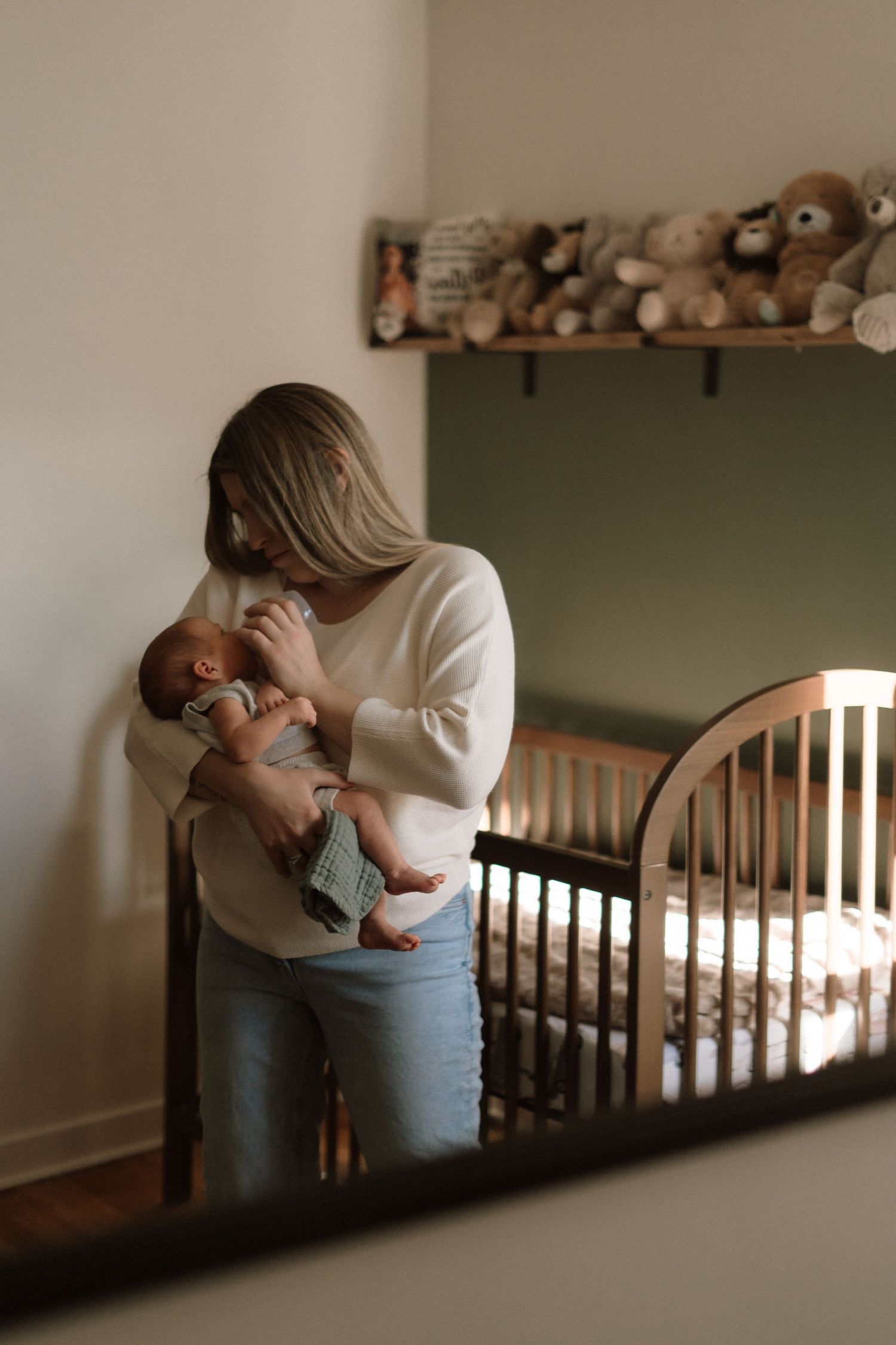 A tender moment in a nursery with a parent holding and comforting a newborn baby next to a wooden crib.