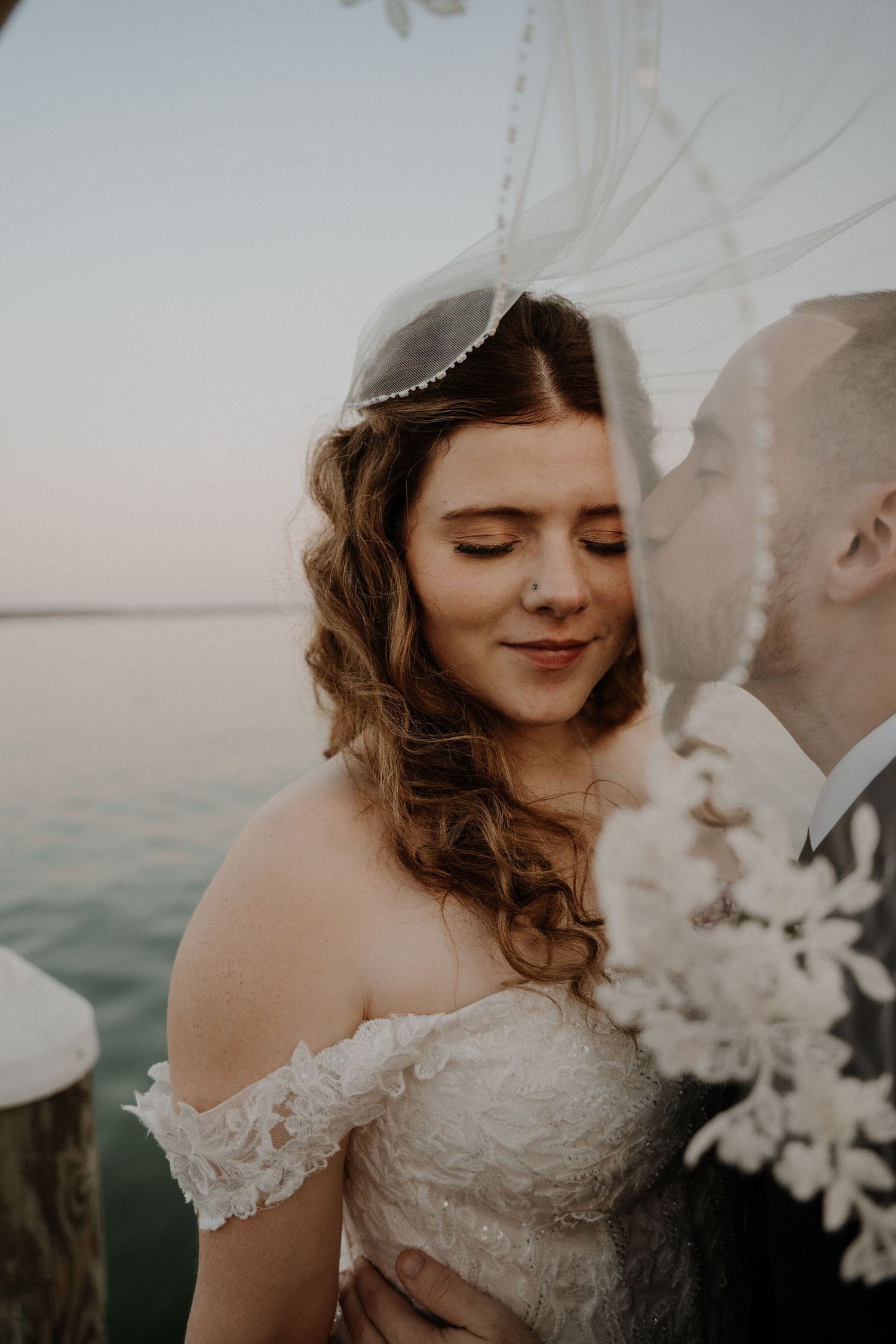 A bride with closed eyes smiles softly during an intimate wedding moment by the water.