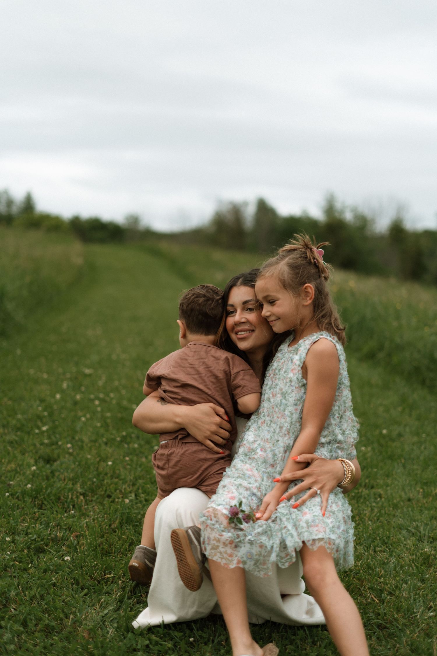 Mother and children sharing a joyful moment together while sitting in a grassy meadow on a cloudy day.