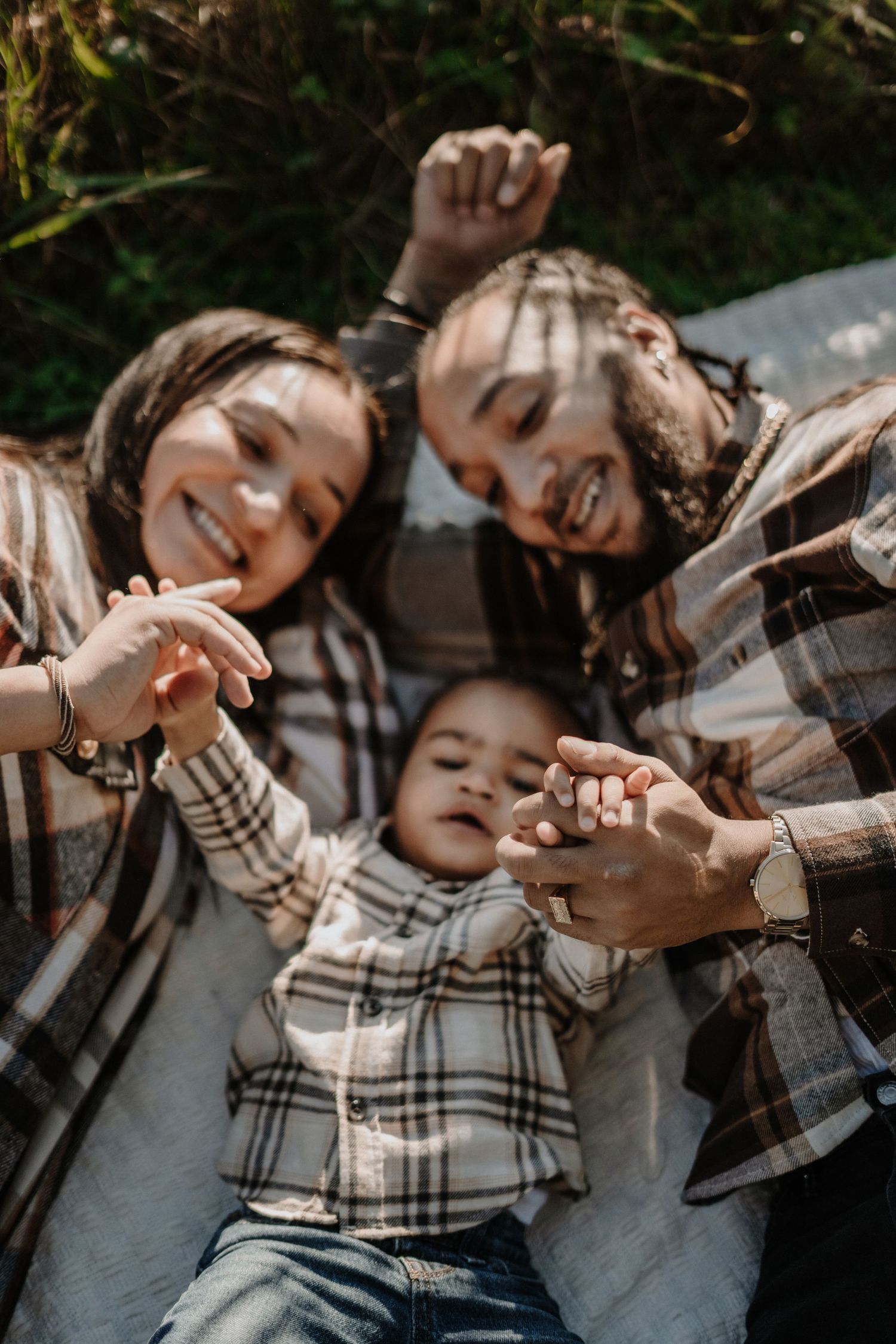 Loving moment with parents and baby captured from above on a blanket outdoors wearing coordinating plaid patterns.