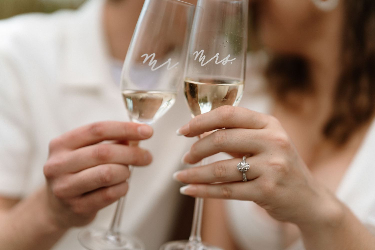 Newlyweds toasting with Mr. and Mrs. champagne flutes, bride wearing diamond engagement ring.