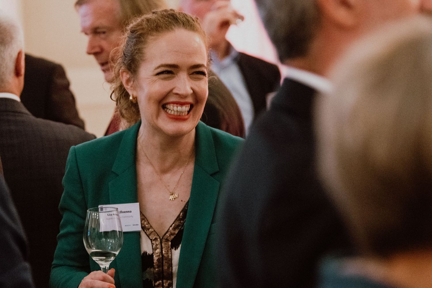Business professional in green blazer enjoying networking event with wine glass.