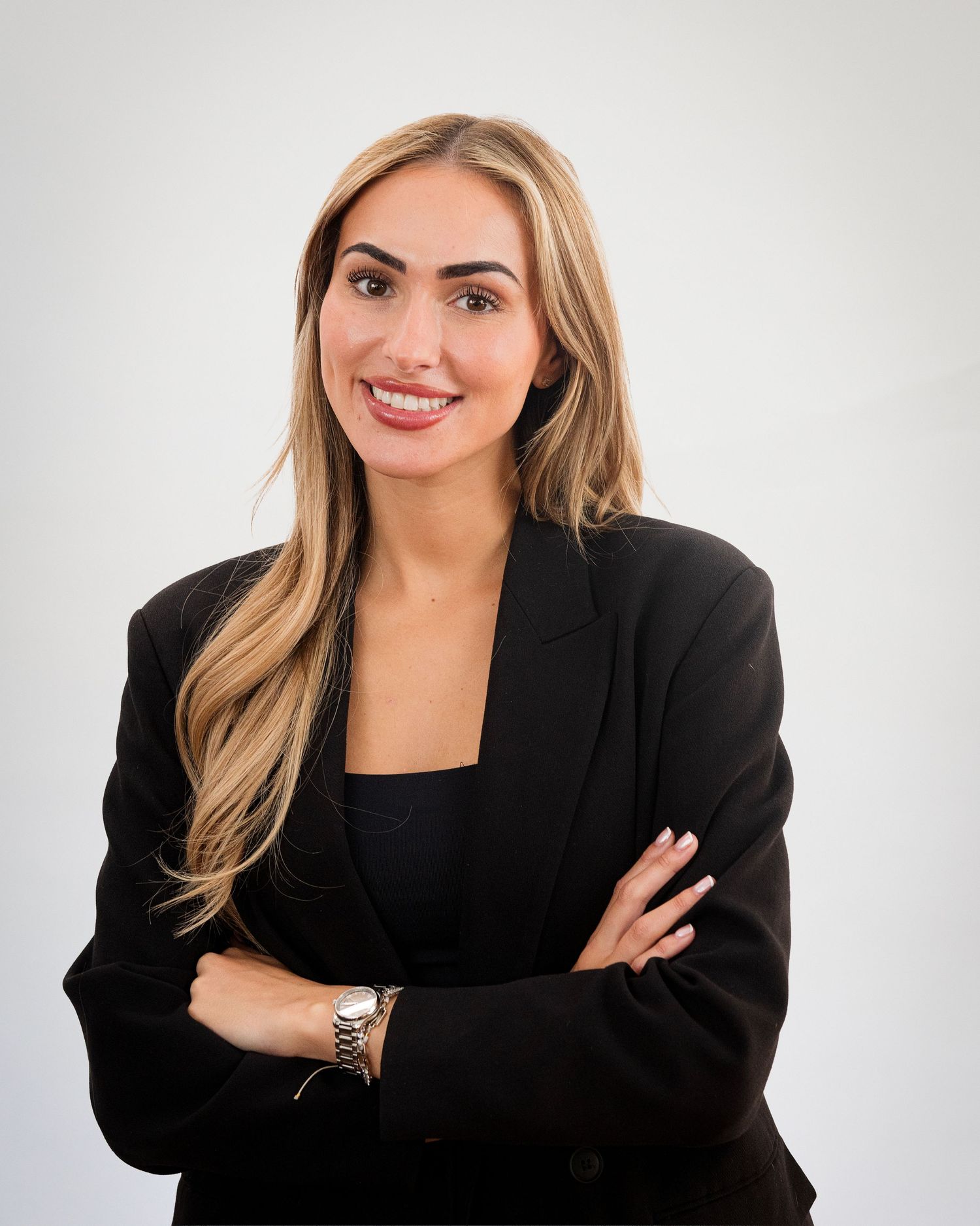 Professional portrait of businesswoman in black blazer with blonde hair against white background.