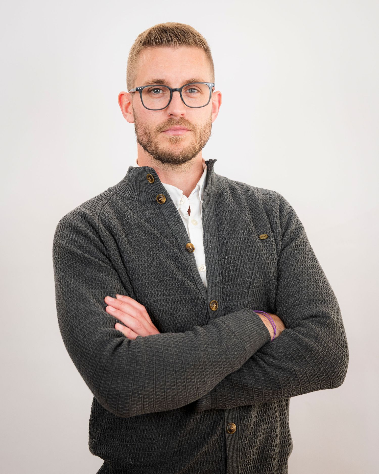 Professional headshot of person in gray cardigan sweater with glasses against white background.