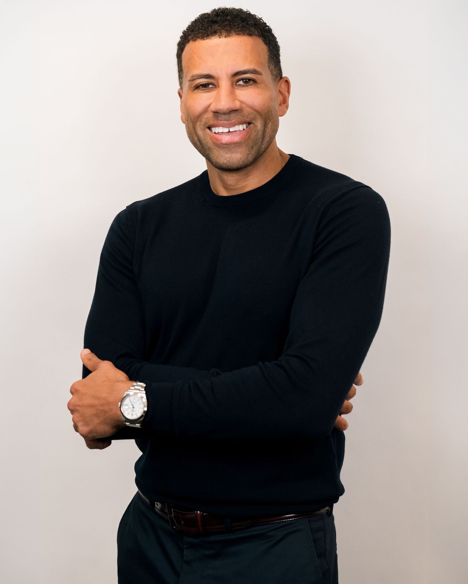 Professional headshot of person in black sweater with bright smile against white background.