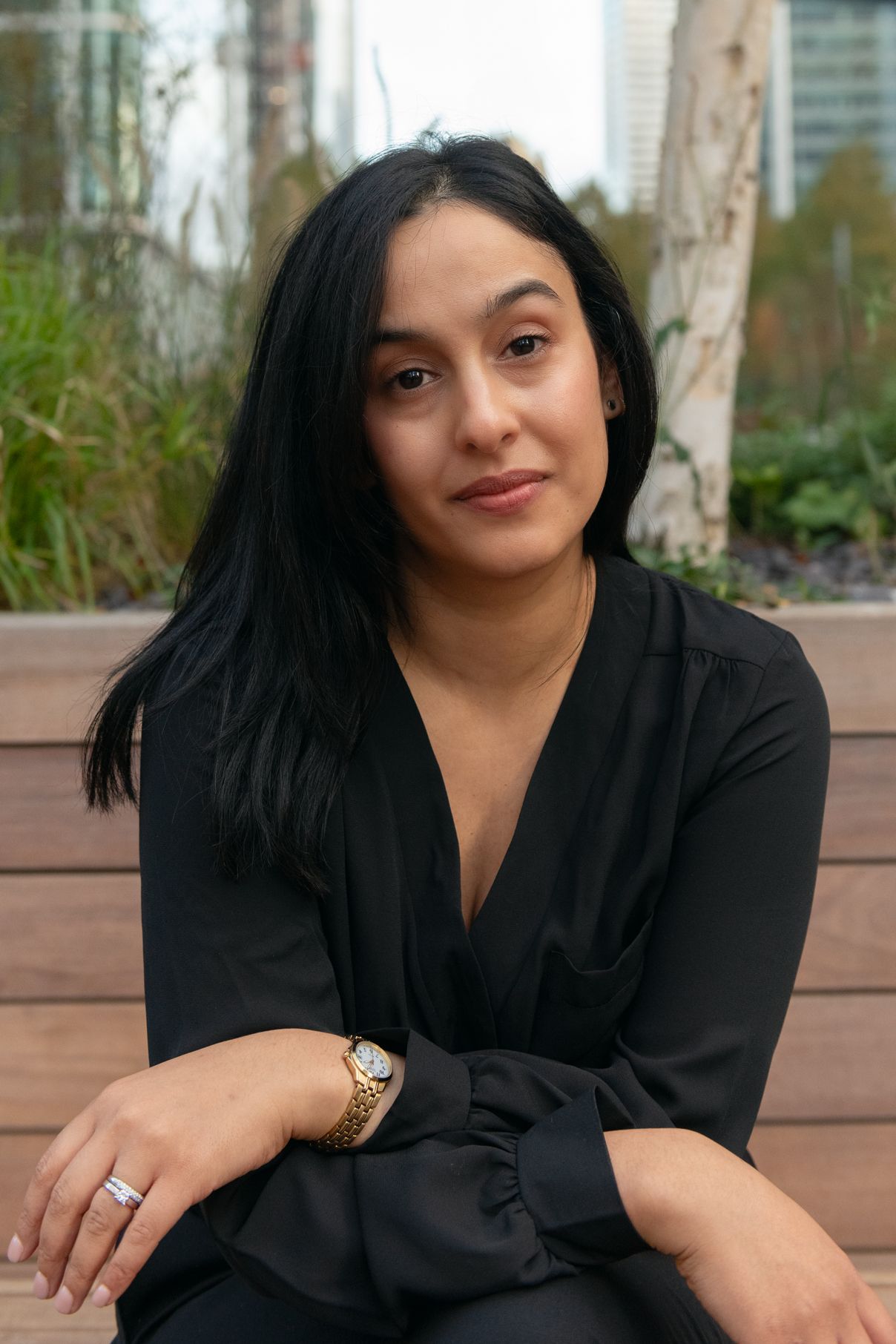 Woman in black blouse sitting outdoors on wooden deck with urban background.