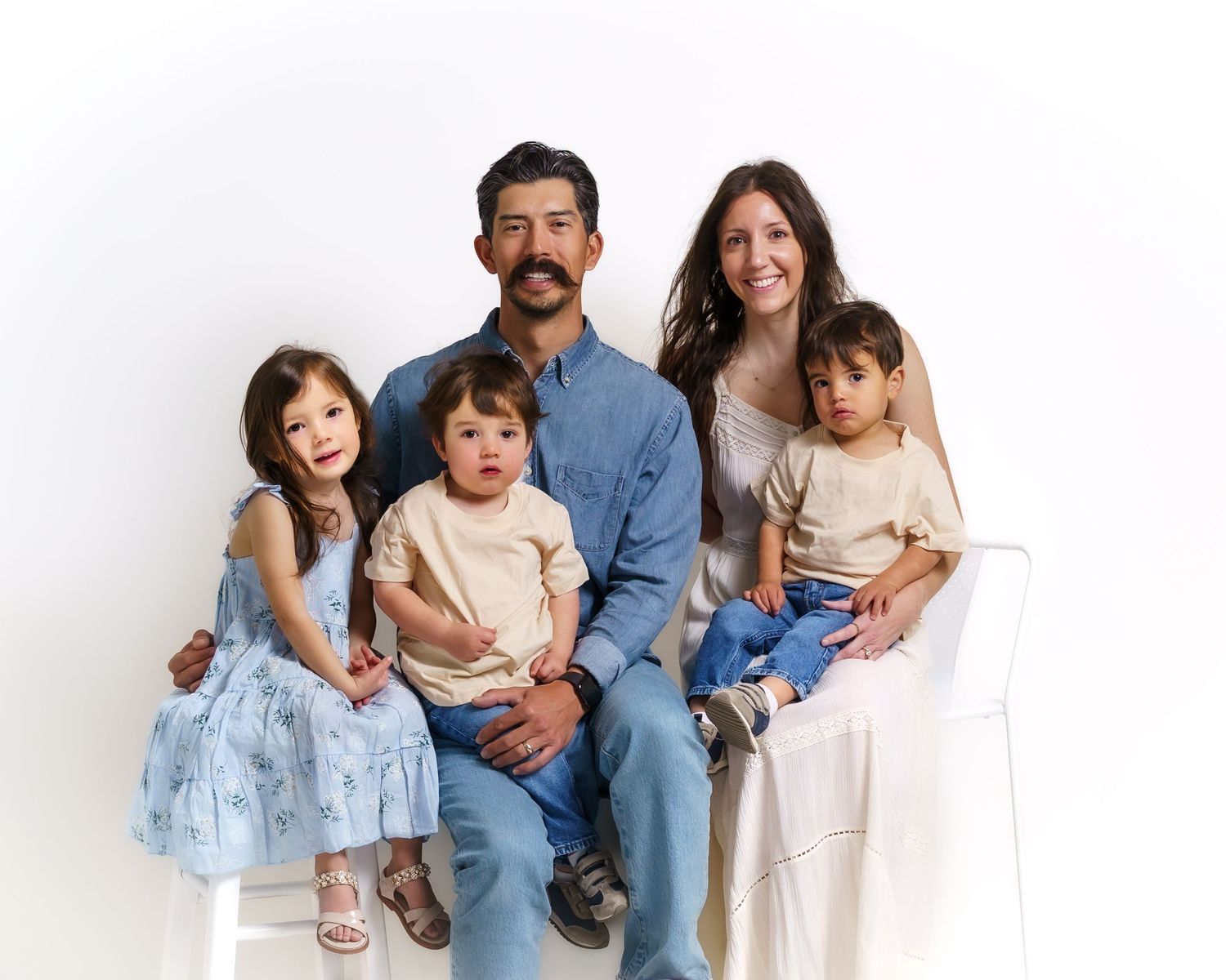 Family of five with father, mother, and three young children sitting together in studio portrait.