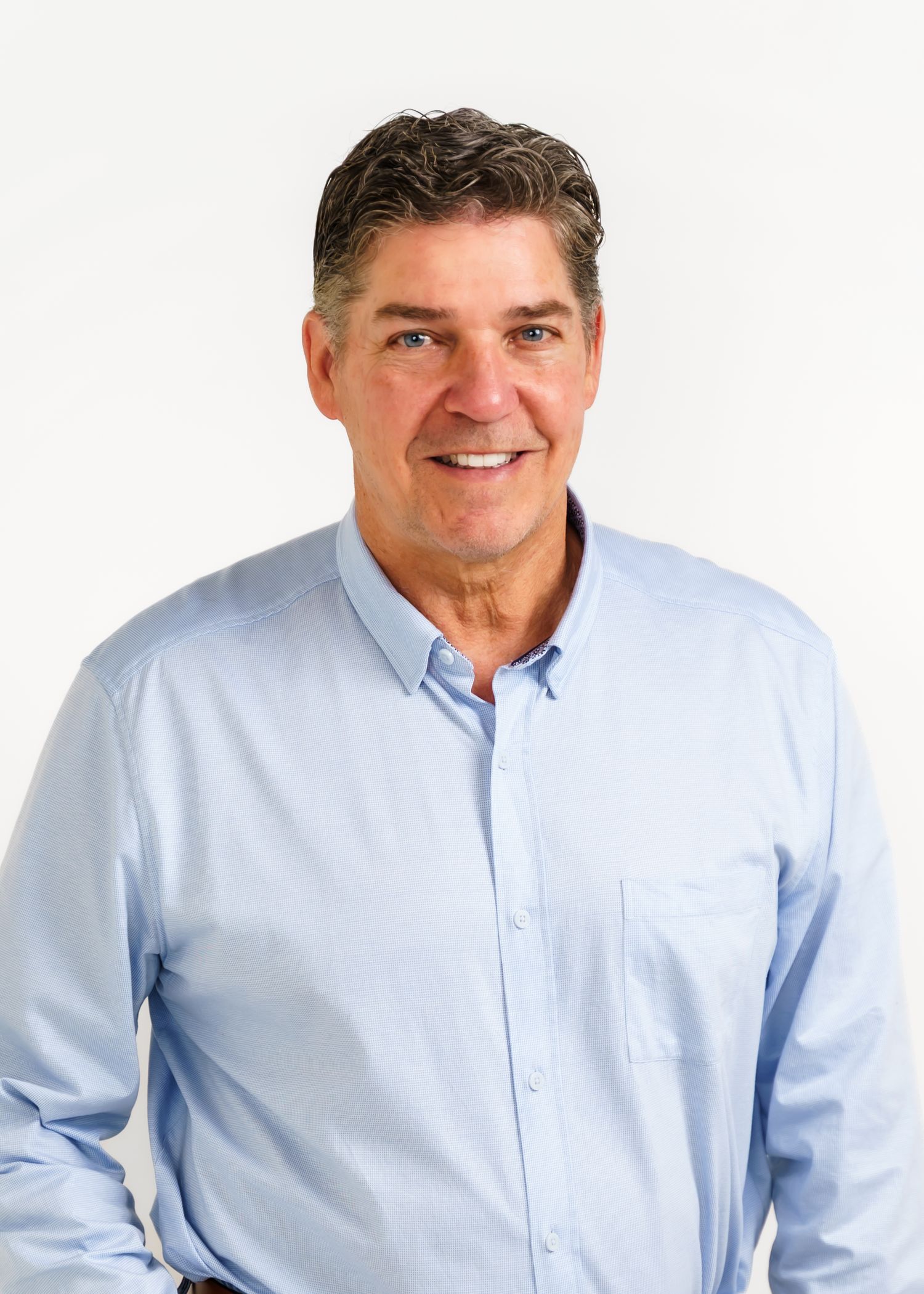 Professional headshot of a smiling middle-aged man in a light blue button-up shirt against a white background.