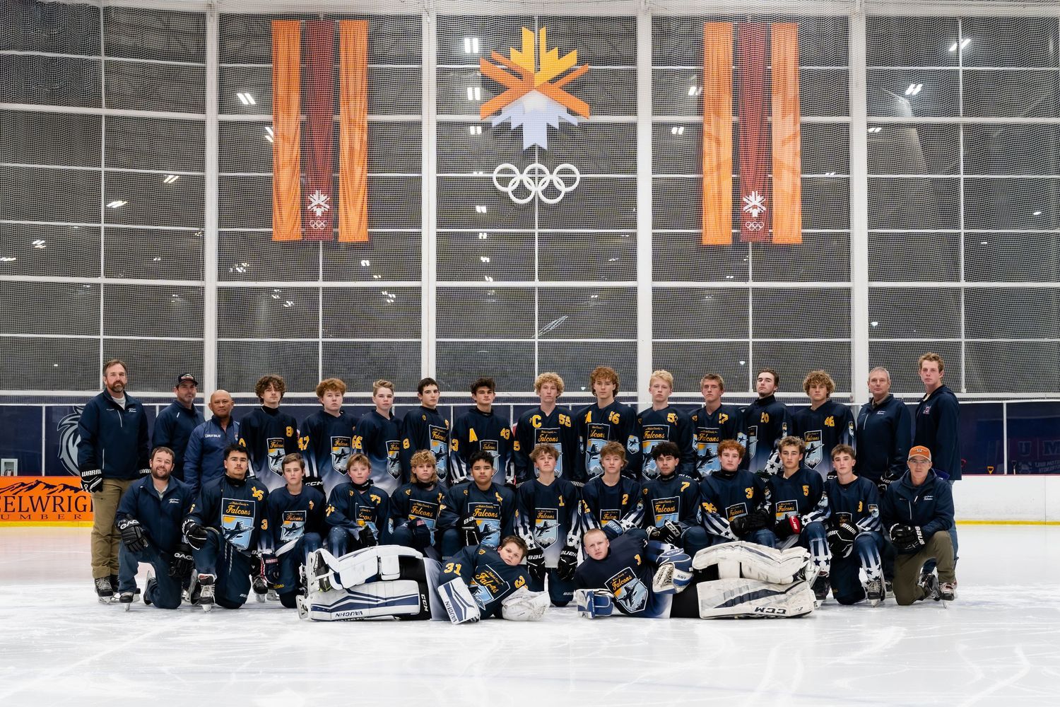 Youth ice hockey team poses for group photo in front of Olympic rings at indoor ice rink arena.