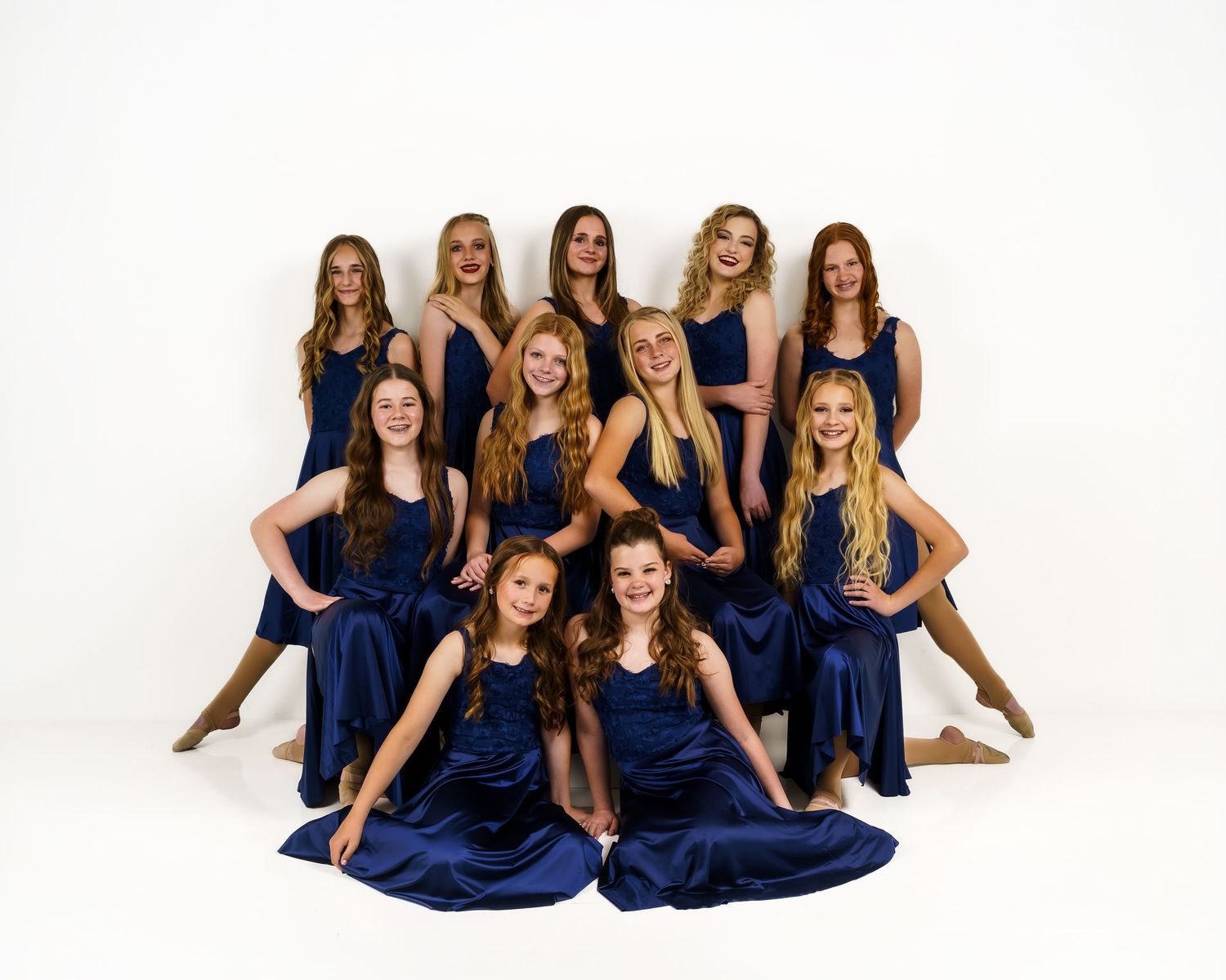 Group of young female dancers in matching navy blue satin dresses posing together in a professional studio photo.