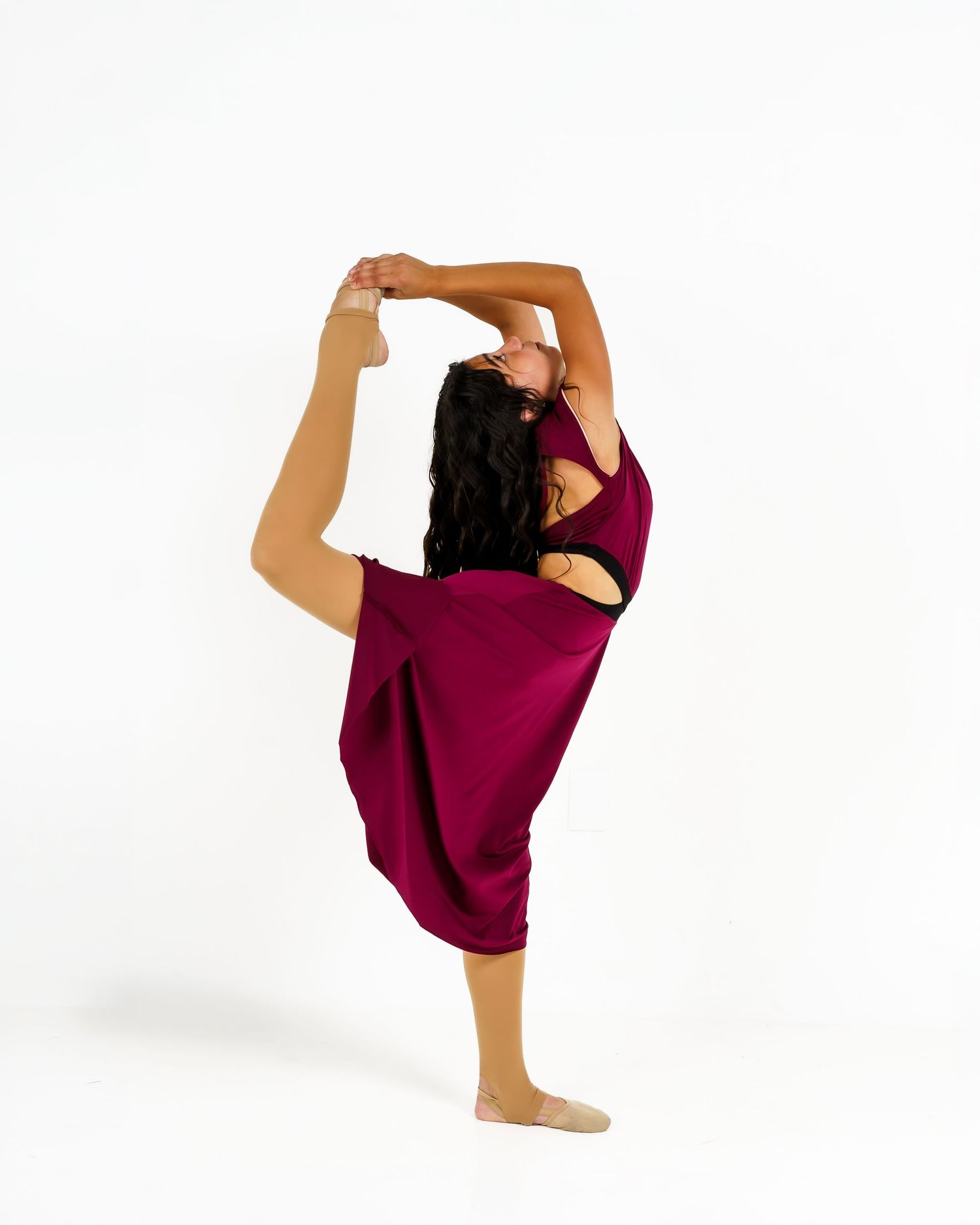 A flexible dancer in a burgundy outfit performs a standing back bend while balancing on one leg against a white background.