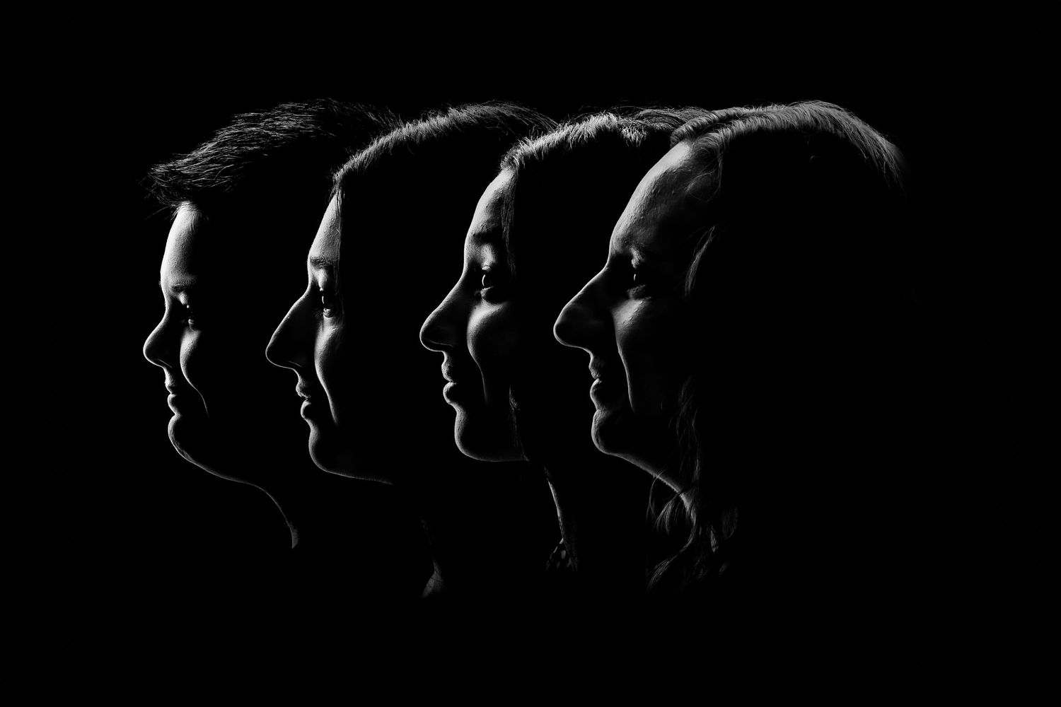 Four people in dramatic black and white profile silhouettes against a dark background.