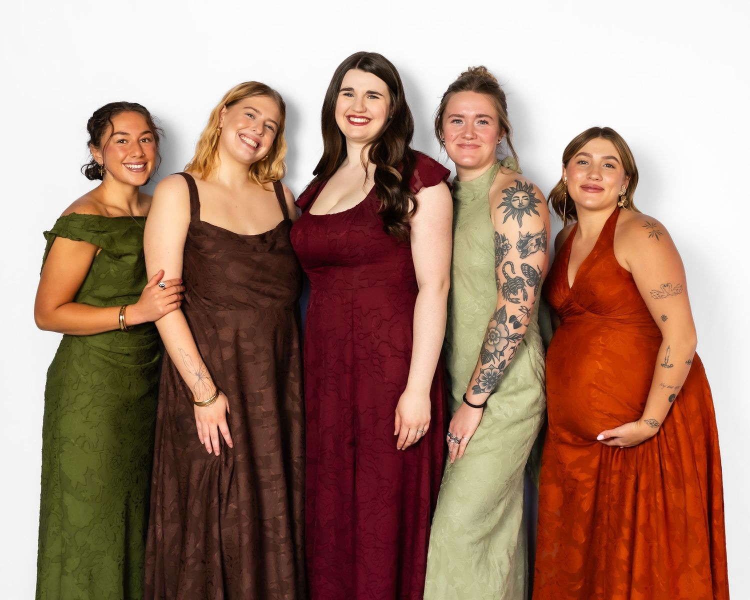 Five women in elegant earth-tone formal gowns posing together, smiling against a white background.