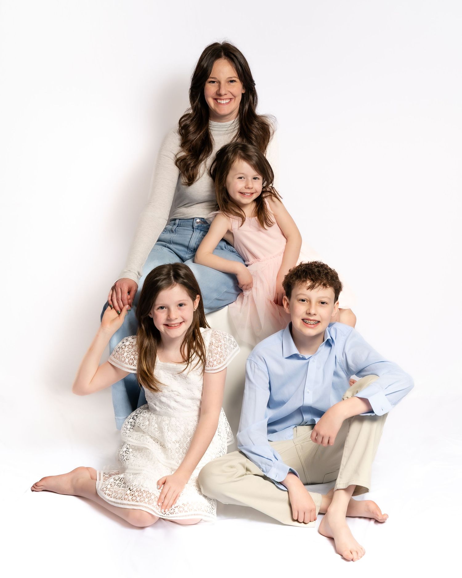 Mother smiles with three children arranged in pyramid pose against clean white studio background.