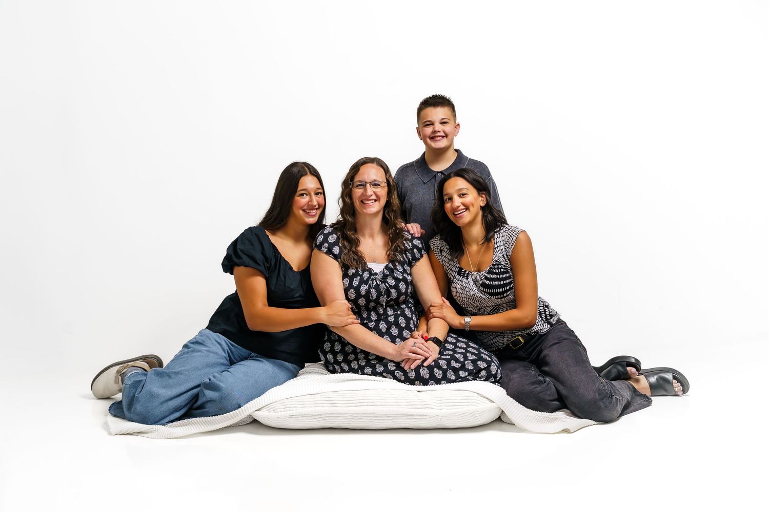 Happy family of four posing together on white background in a professional portrait studio photo.
