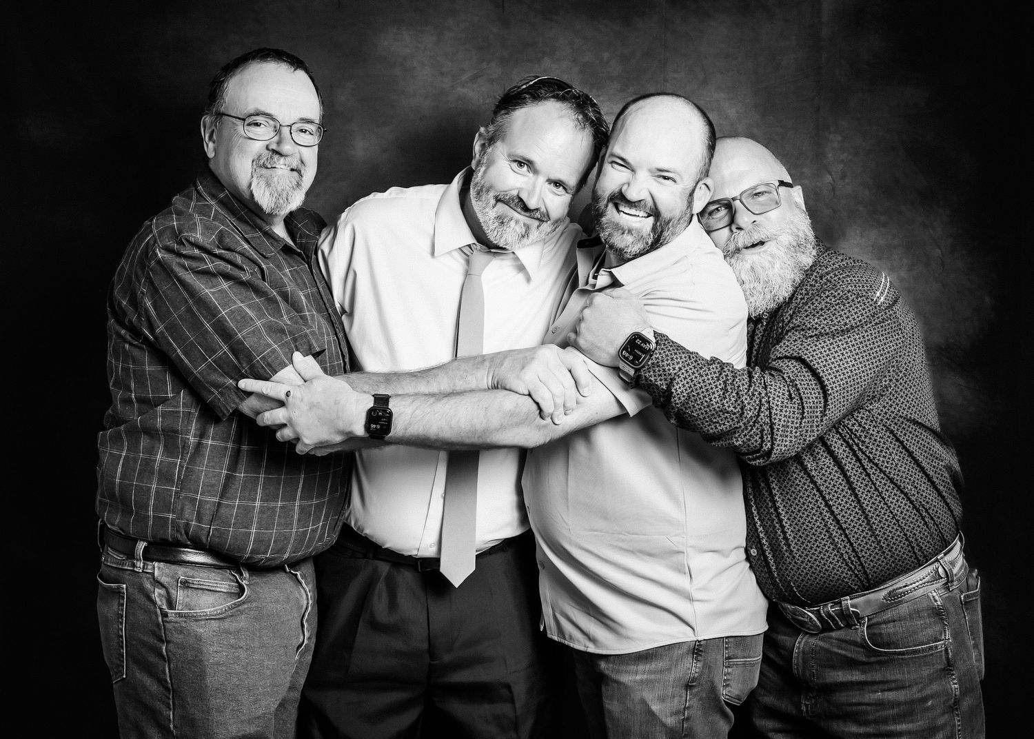 Four men hugging and smiling together in a black and white studio portrait photo.