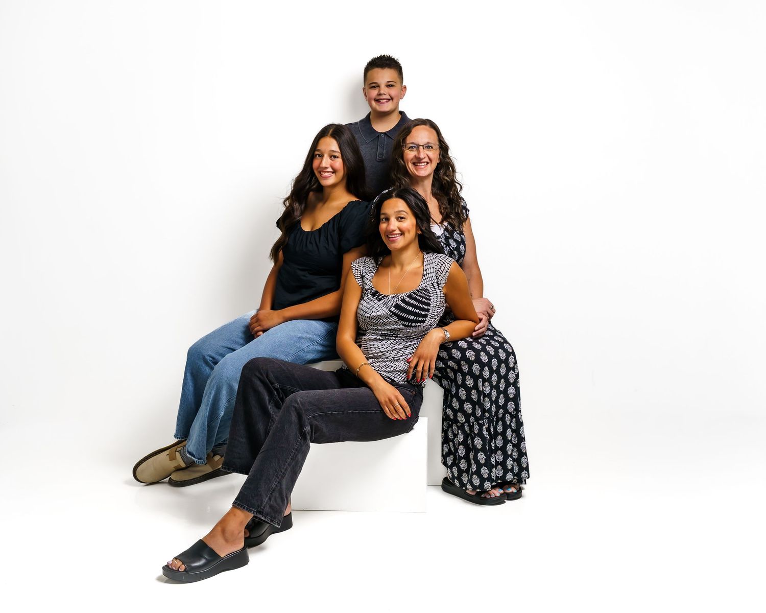 A family of four poses together for a portrait, with three girls and a boy, against a white background.
