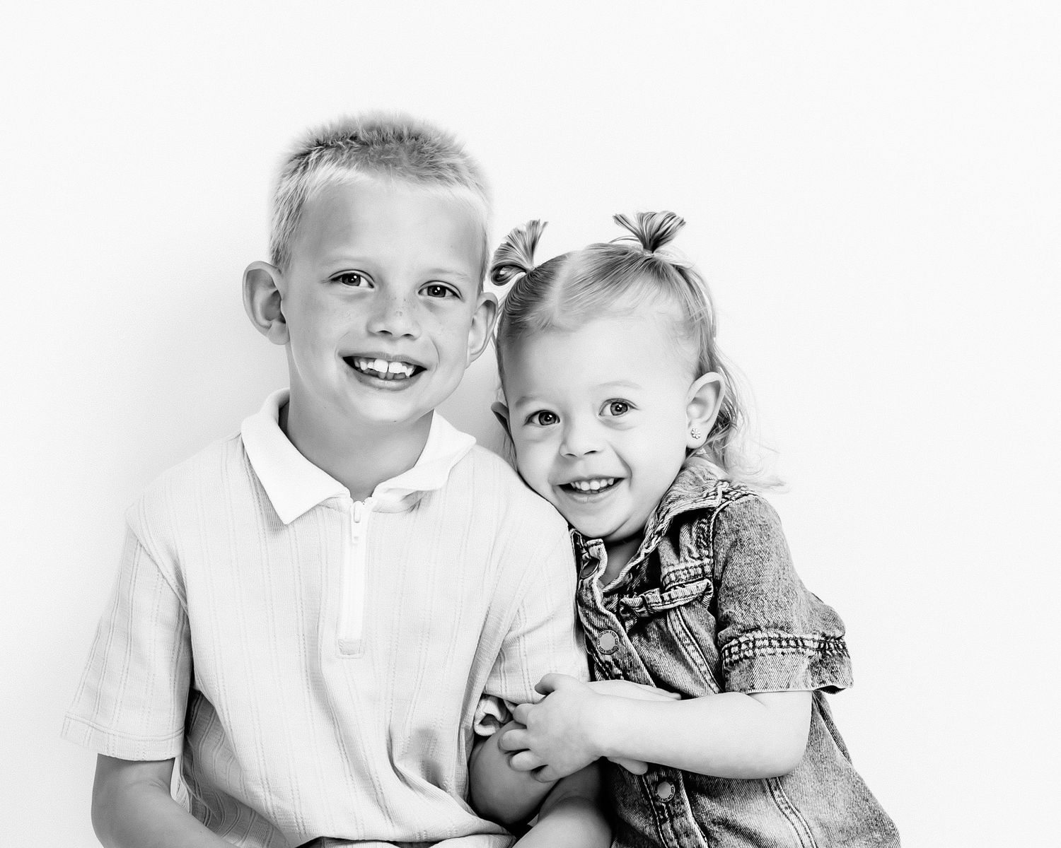 Happy siblings boy and toddler girl hugging and smiling in black and white studio portrait.