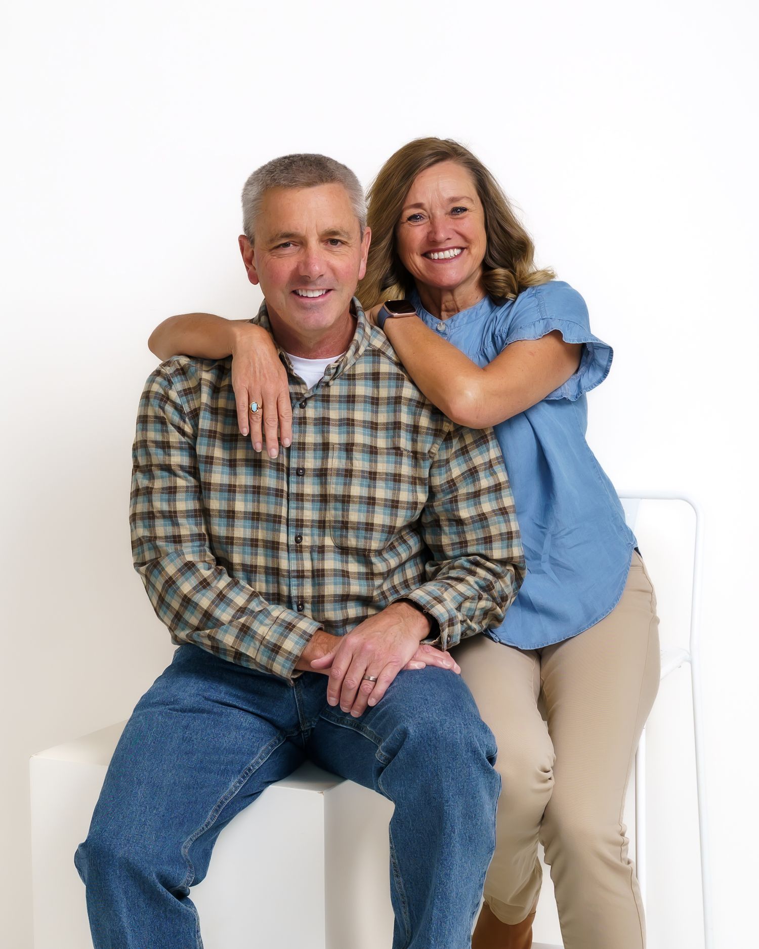 Smiling middle-aged couple posing together in casual attire for a bright white studio portrait.