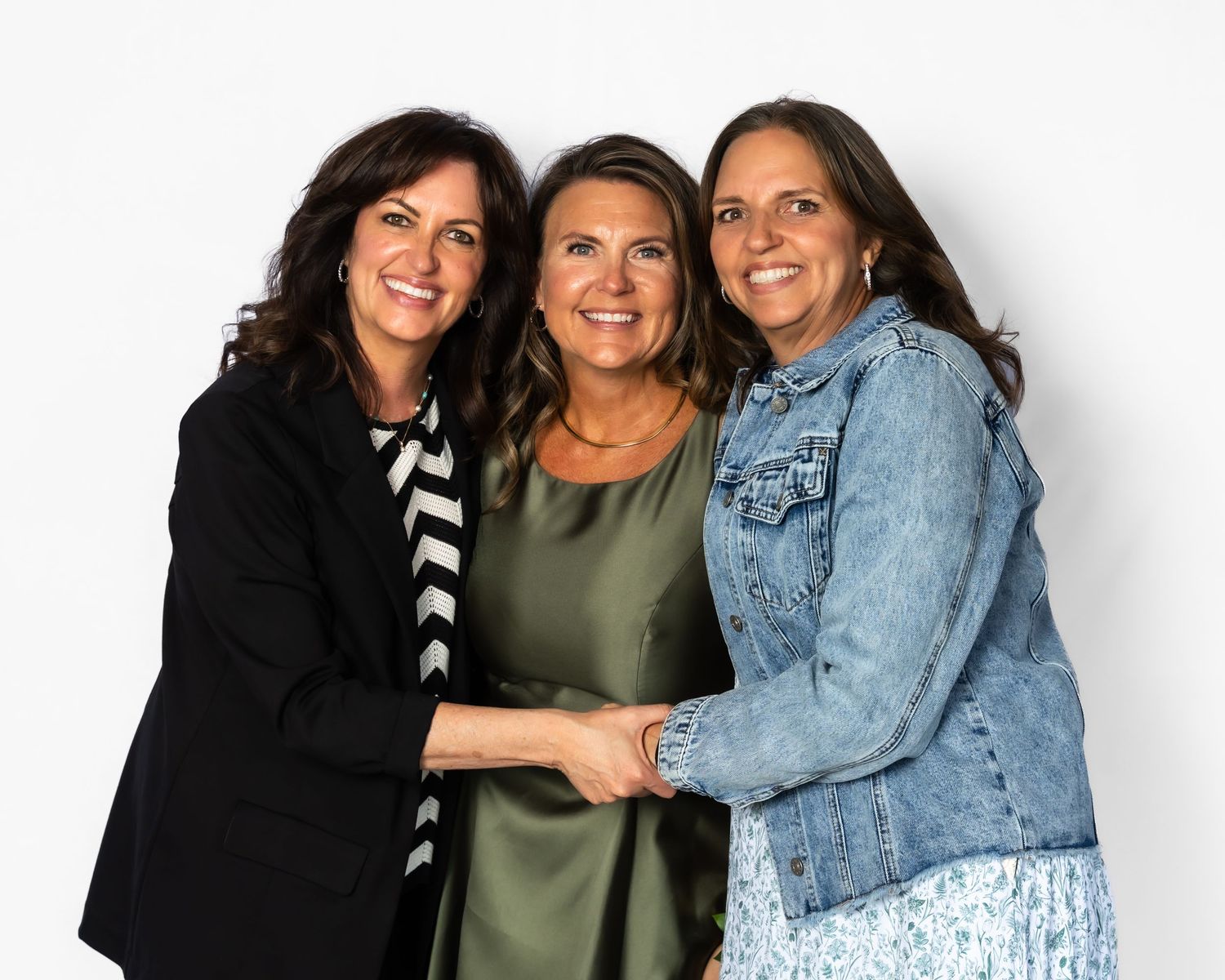 Three smiling women pose together for a professional portrait against a white background.