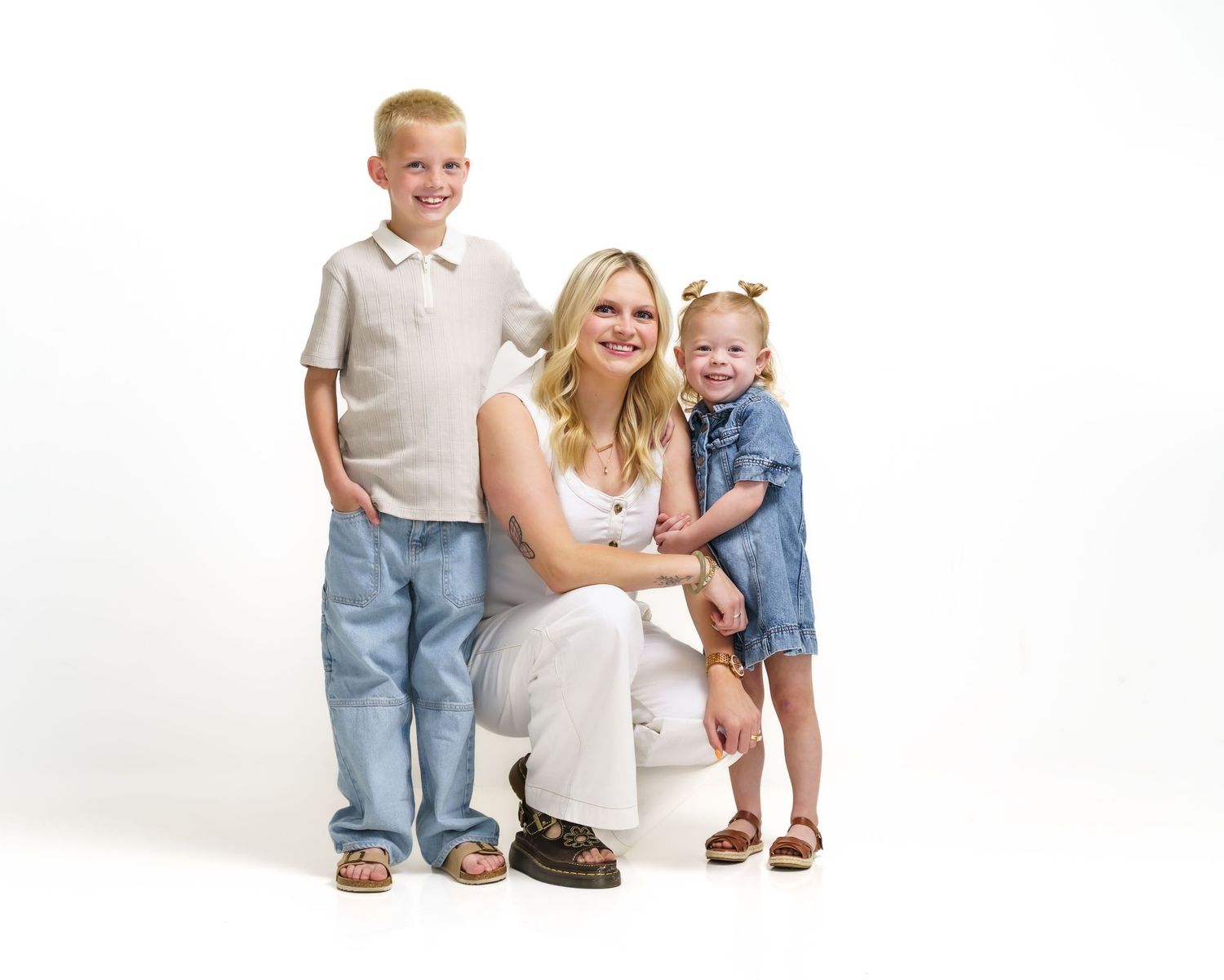 Mother kneeling between young son and toddler daughter in bright studio family portrait.