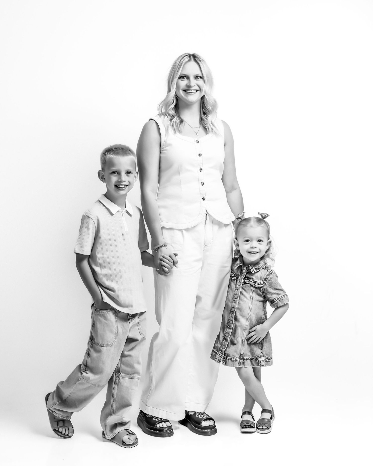 Black and white studio portrait of smiling mother standing with young son and toddler daughter.